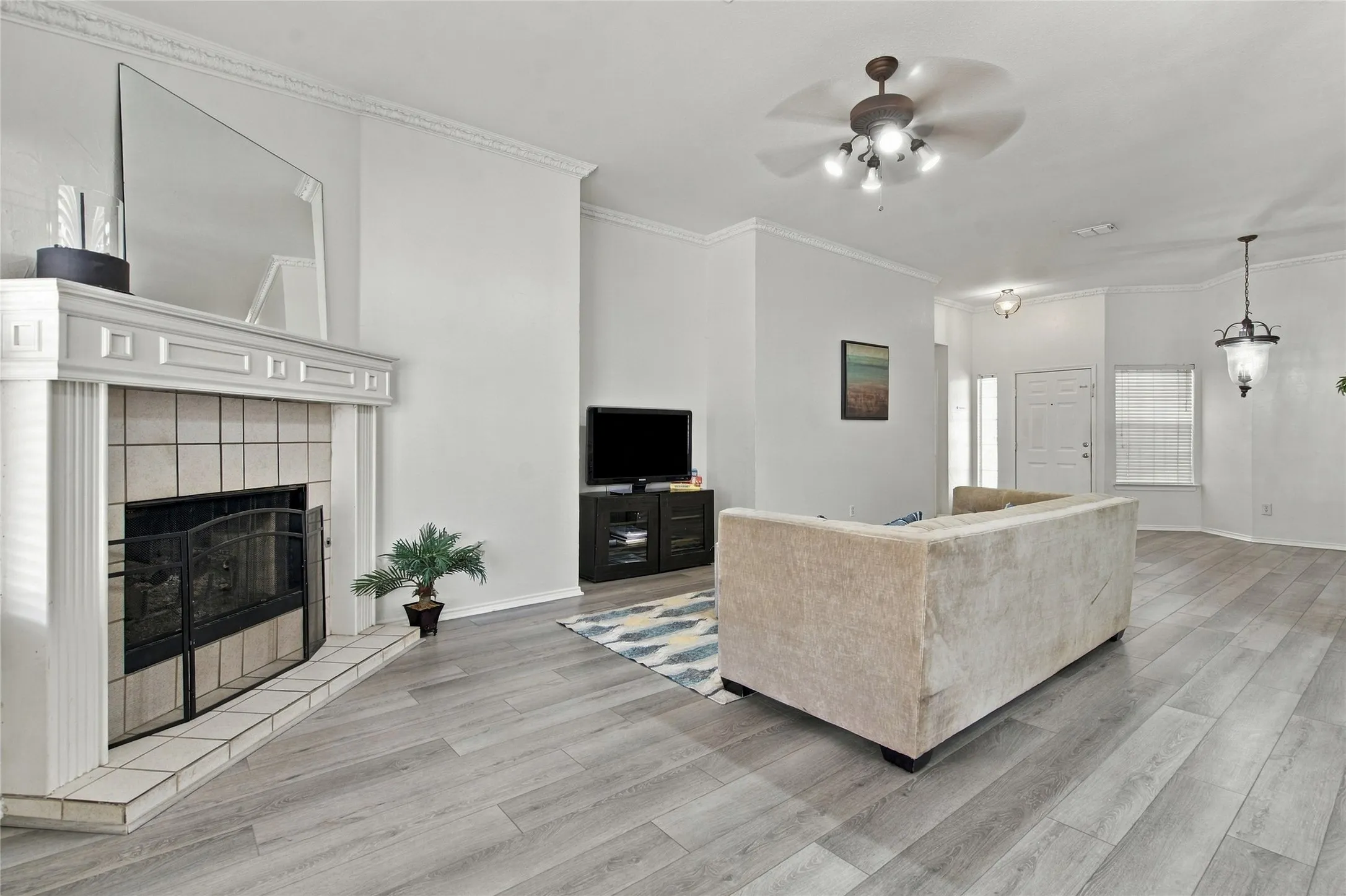 Wood-finish flooring, fireplace with tile surround and mantel, crown molding, ceiling fan, and pendant lighting