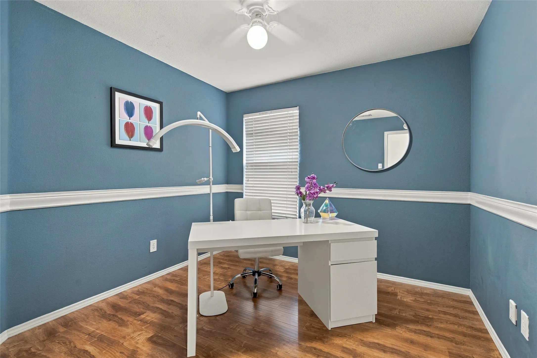 Wood-finish flooring, accent wall molding, ceiling fan with integrated lighting, and window blinds