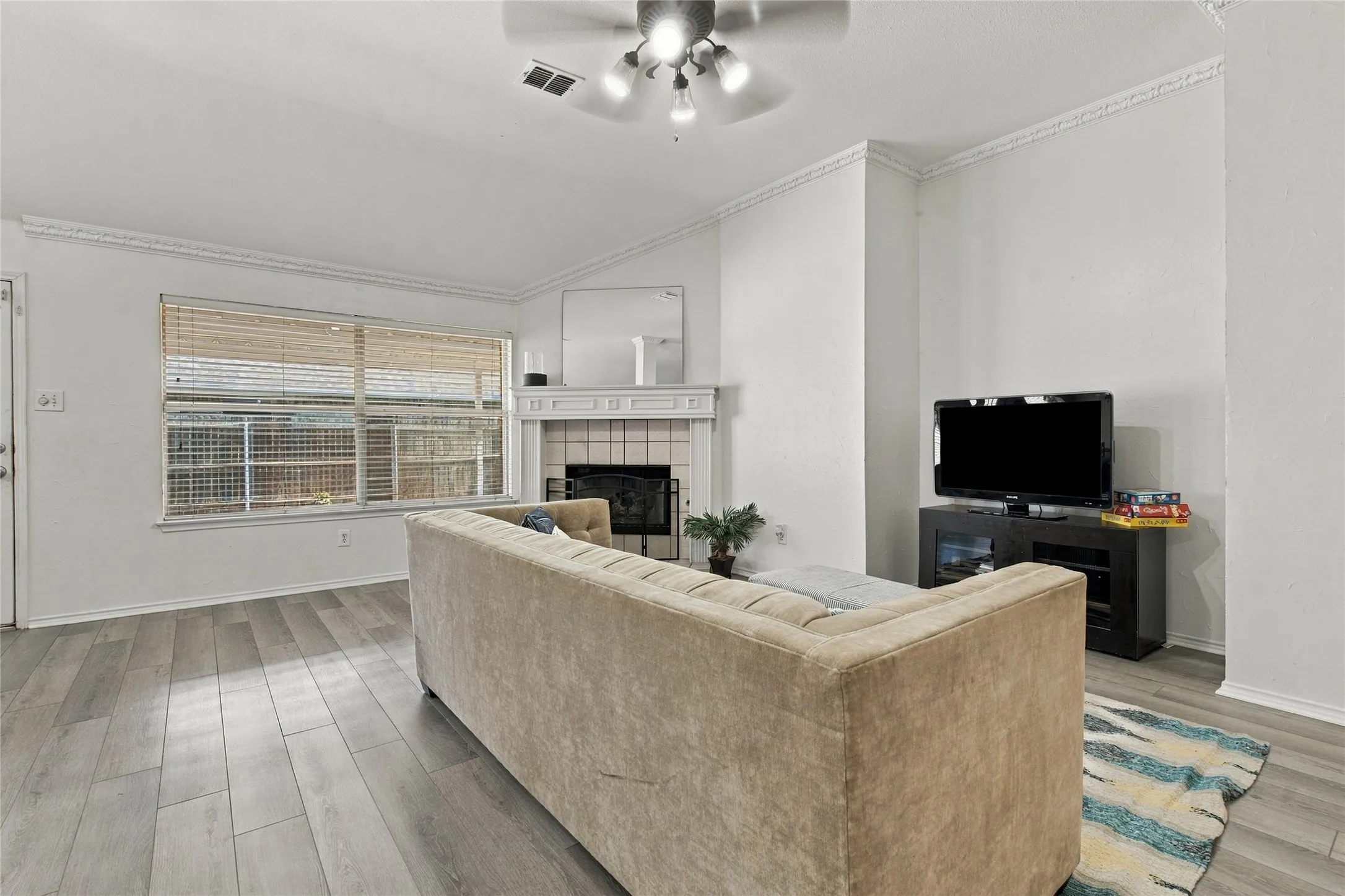 Vaulted ceiling with a ceiling fan, wood-finish flooring, fireplace with tile surround, and crown molding