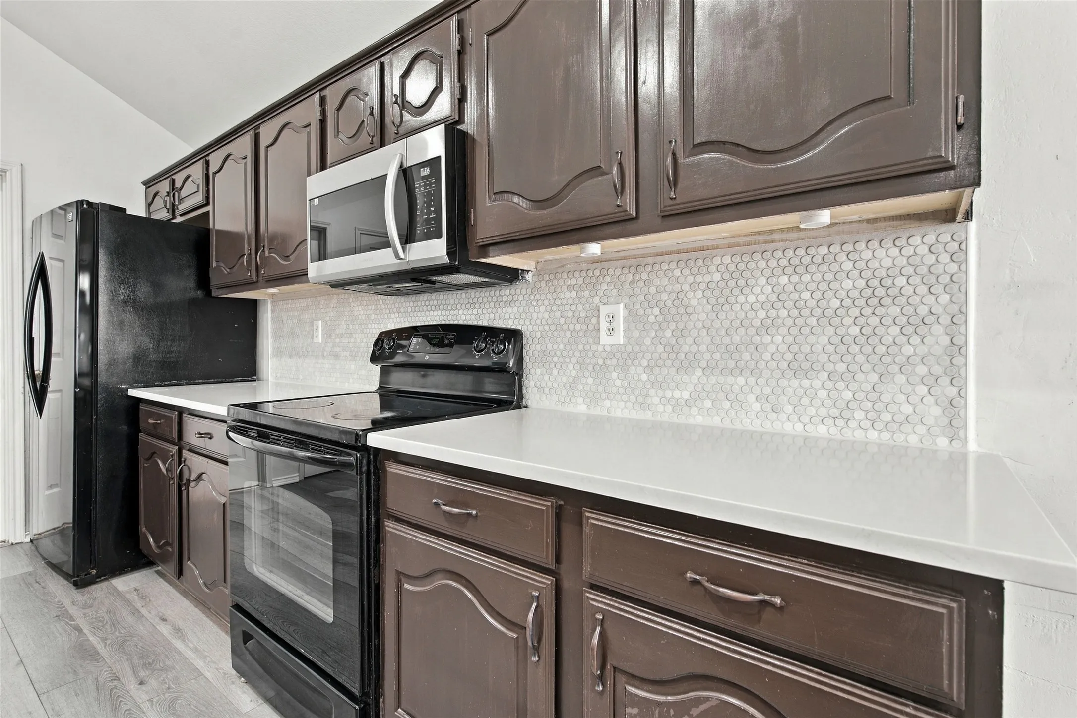 Kitchen with dark wood cabinetry, white countertops, and a white penny tile backsplash