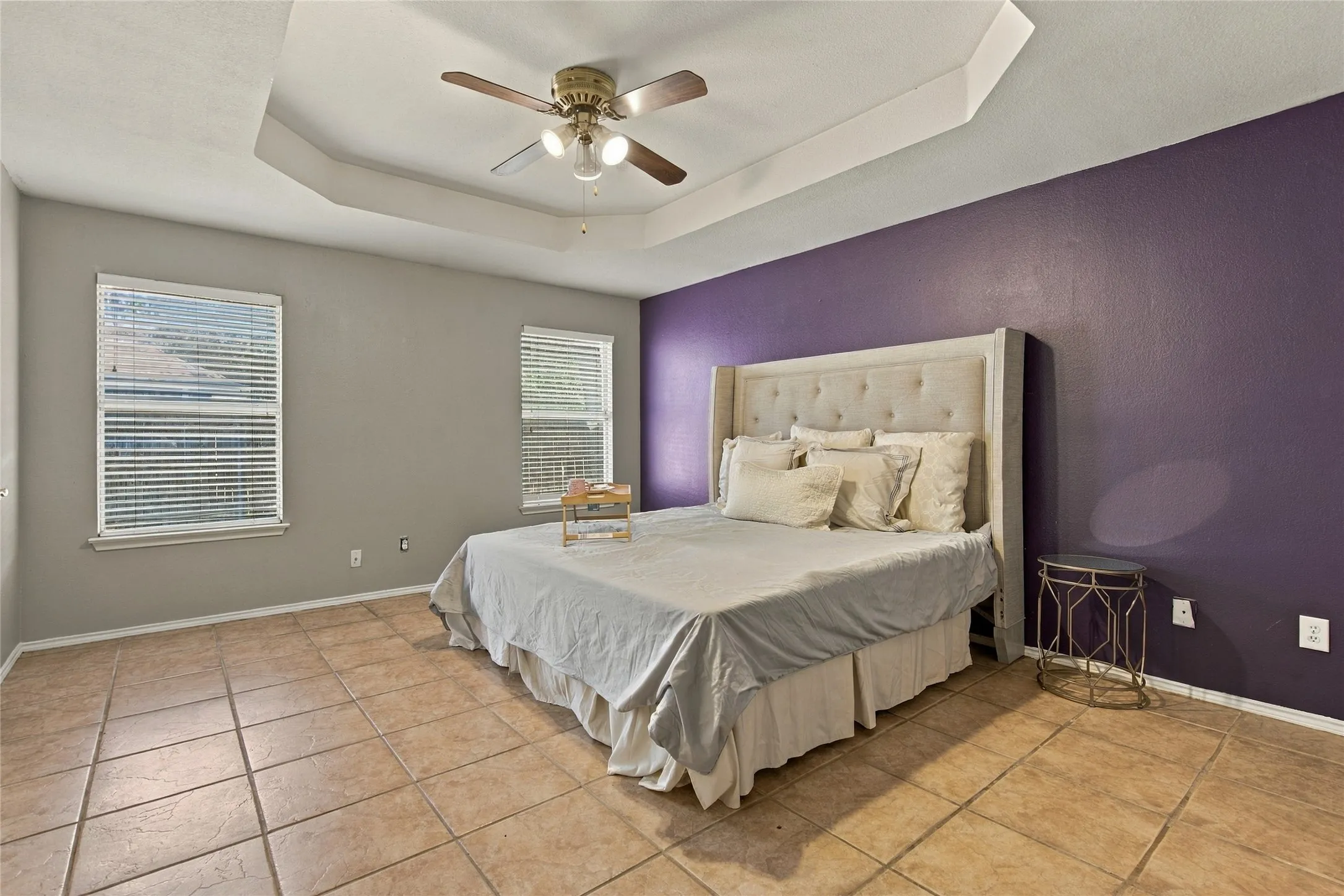 Tray ceiling with a ceiling fan, two windows, and tile flooring