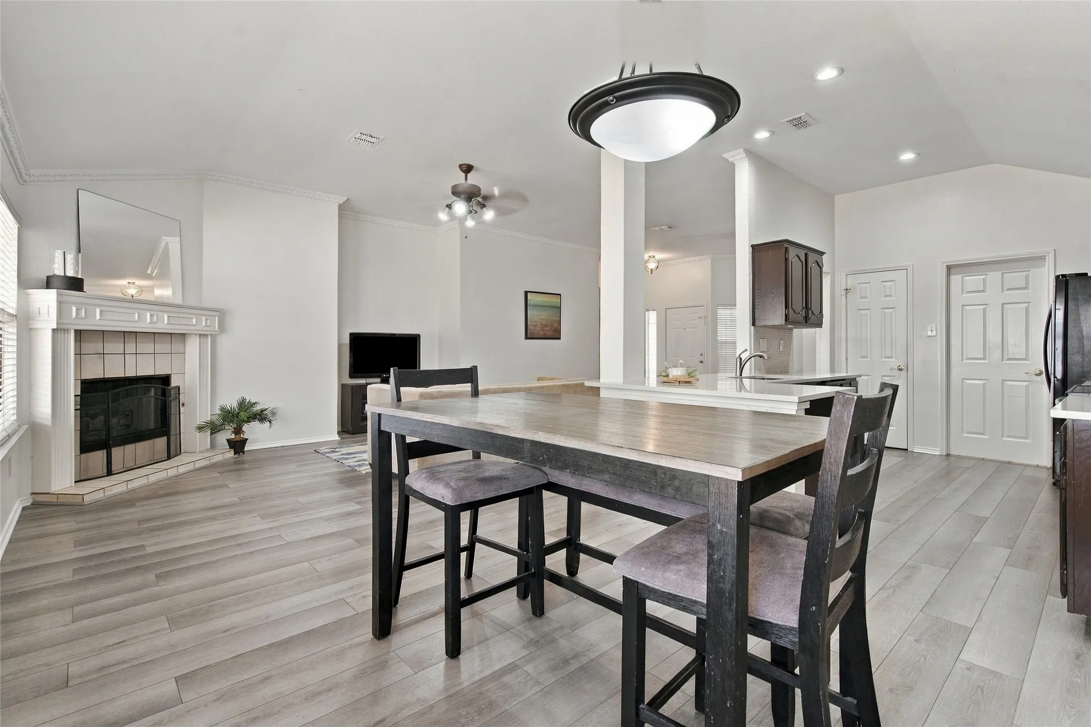 Open-concept living area featuring high vaulted ceilings, wood-finish flooring, a white mantel fireplace, and a kitchen island with a breakfast bar