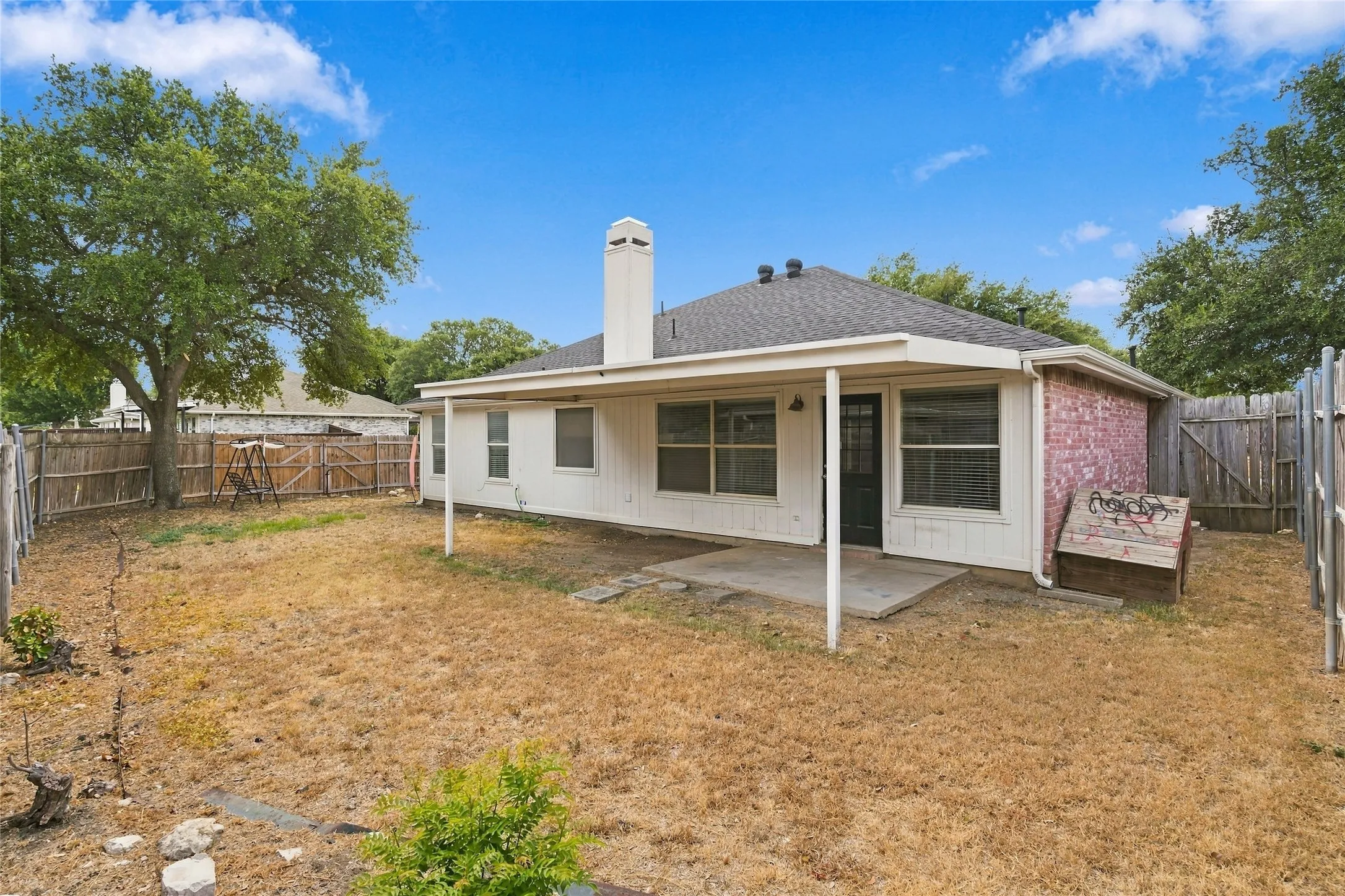 Spacious single-story residence with a covered porch and extended eaves, situated on a generous lot with mature landscaping and wooden perimeter fencing