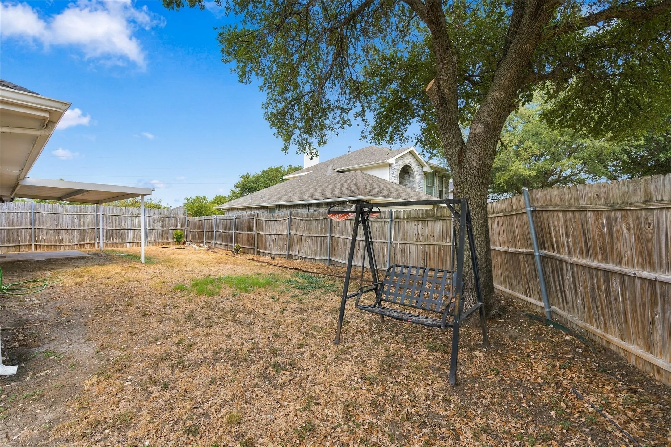 Expansive backyard featuring a large tree, perimeter wood fencing, and a covered patio structure