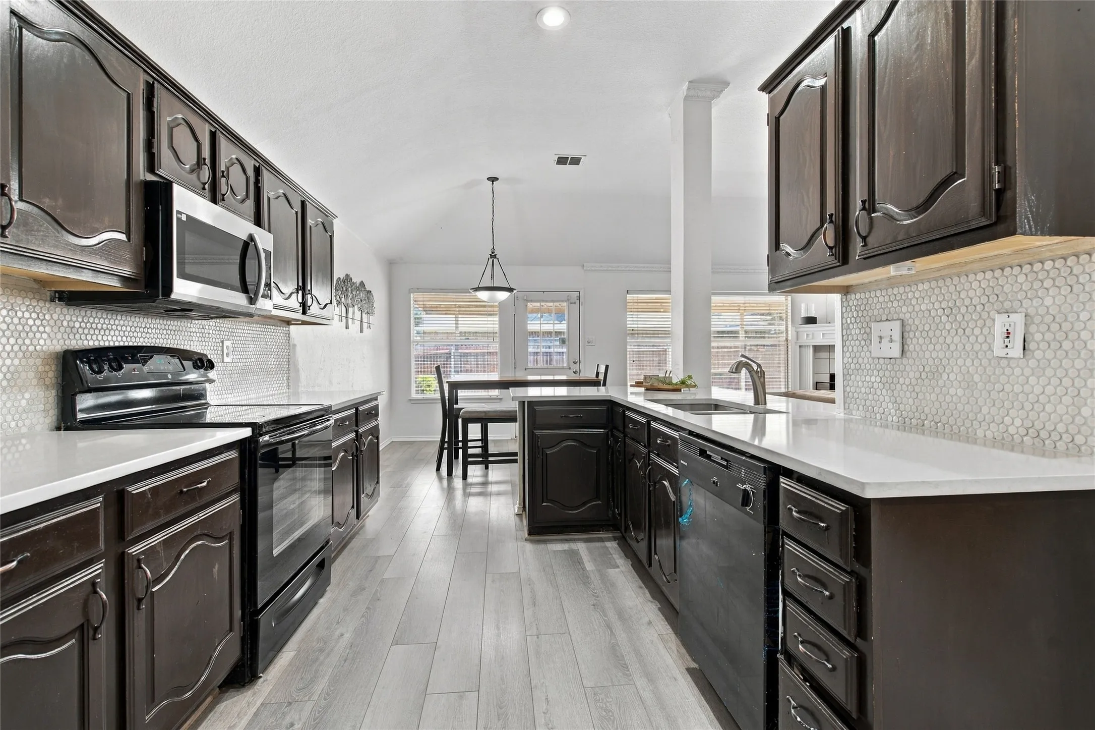 Kitchen featuring dark wood cabinetry, light-toned countertops, a white hexagonal tile backsplash, stainless steel microwave, and wood-finish flooring