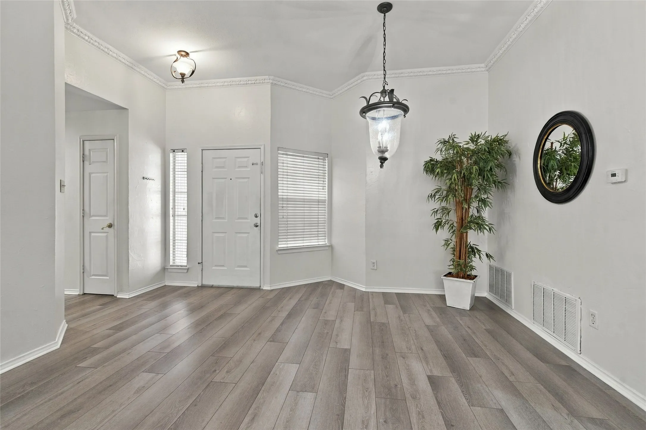 Wood-finish flooring, crown molding, and a decorative pendant light fixture