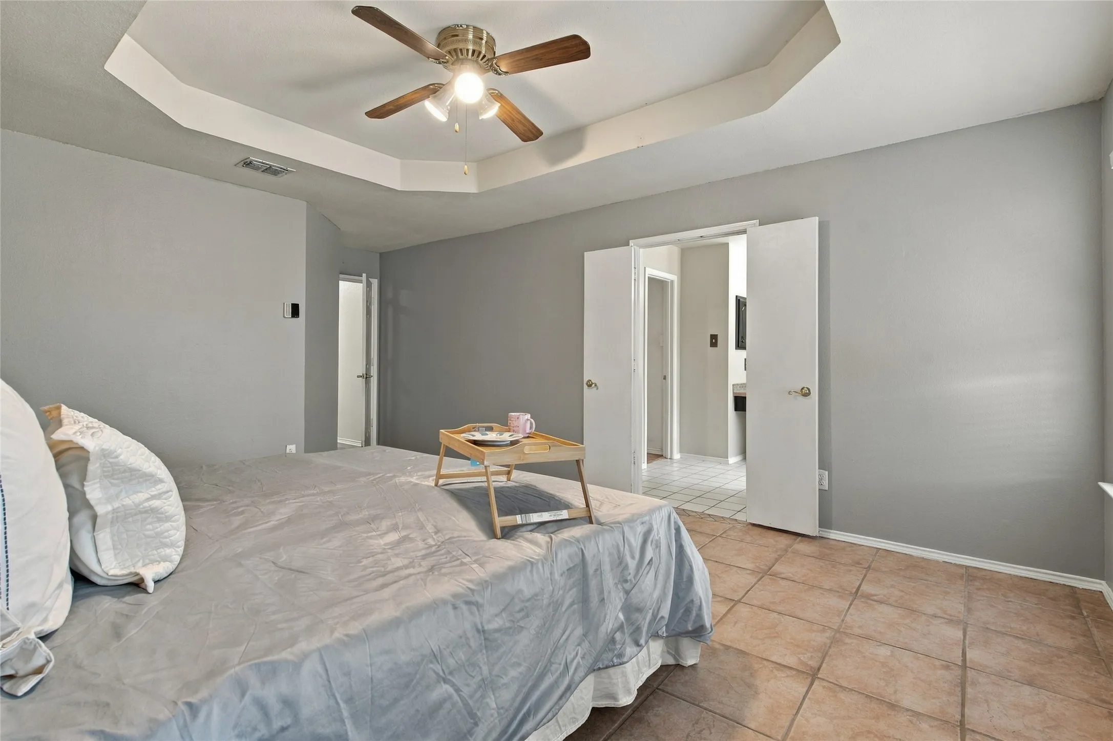 Tray ceiling with a ceiling fan, light gray wall paint, and tile flooring