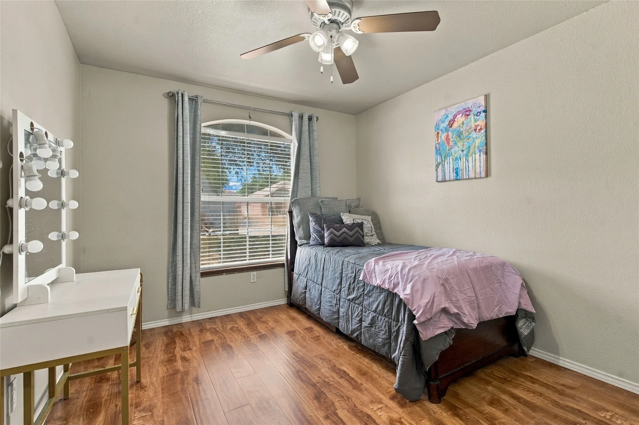 Room featuring wood-finish flooring, a ceiling fan with light fixture, and a window with blinds