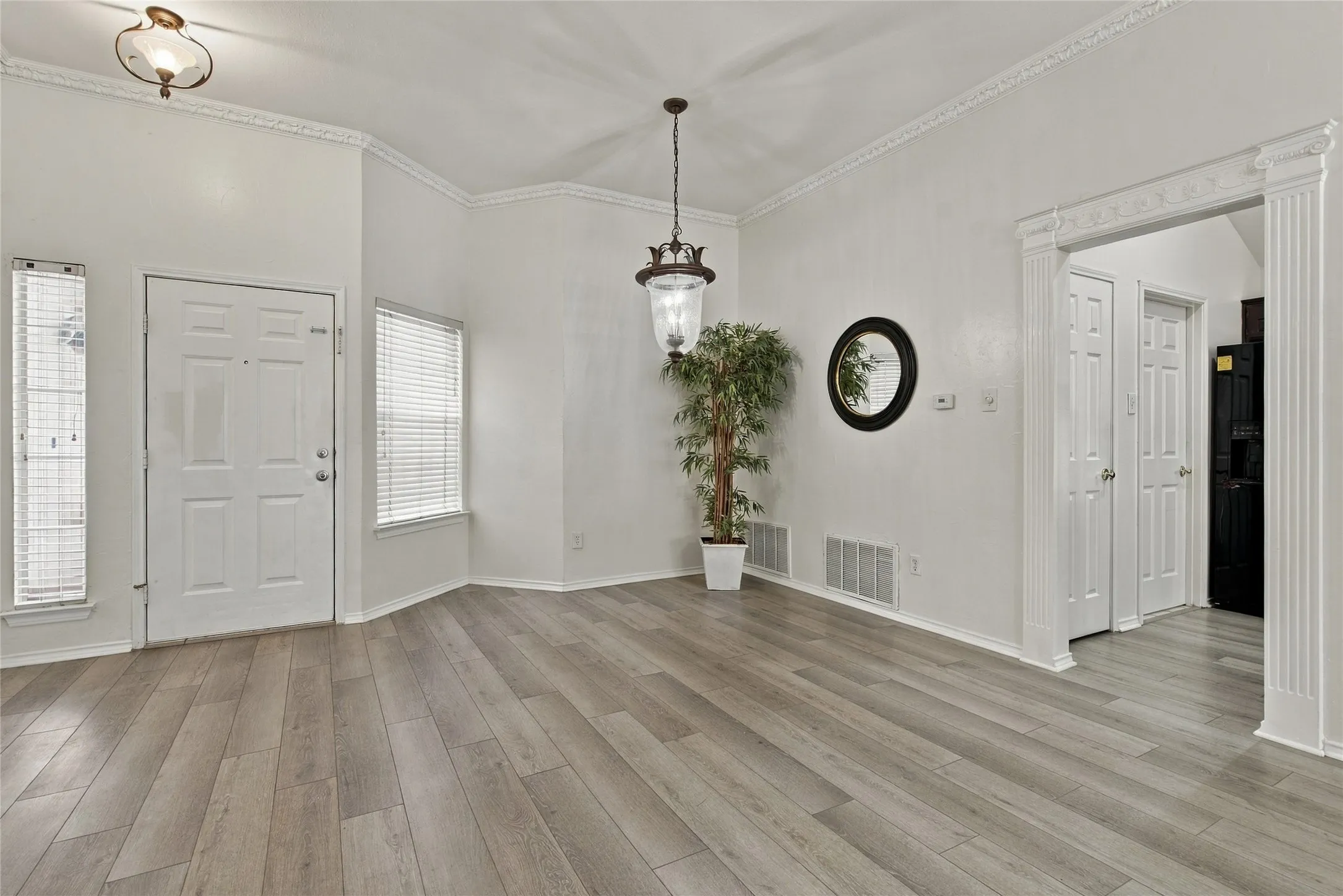 Vaulted ceiling with decorative crown molding, wood-finish flooring, two large windows with blinds, and a decorative archway
