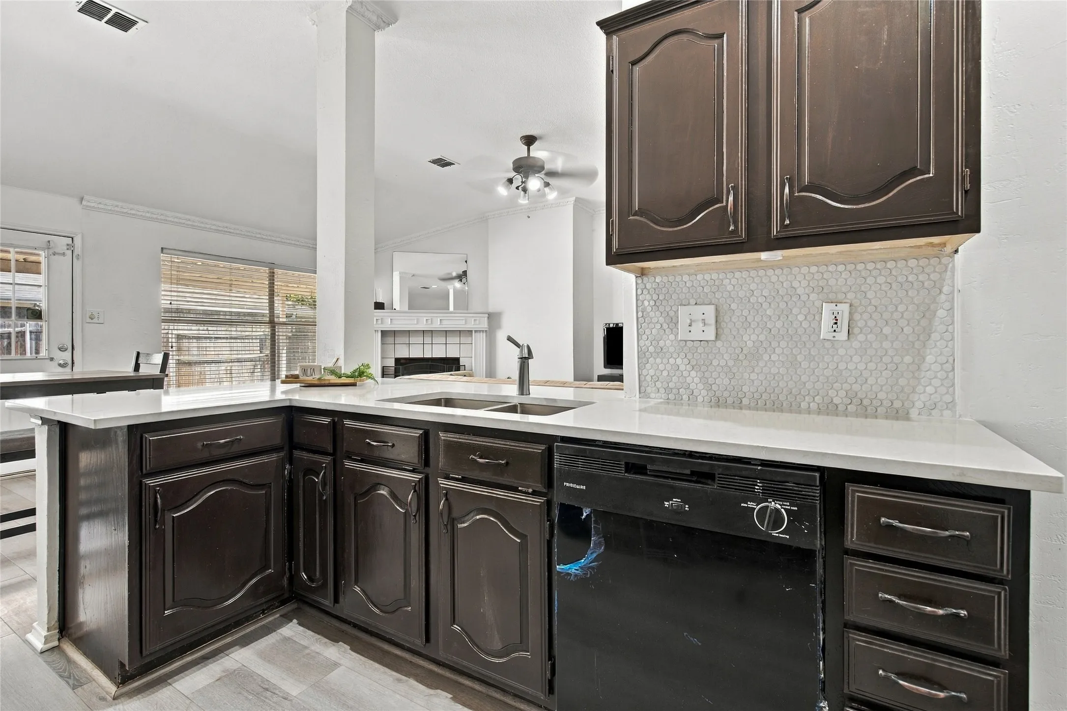 Kitchen featuring dark wood cabinetry, white countertops, a mosaic tile backsplash, and a built-in dishwasher