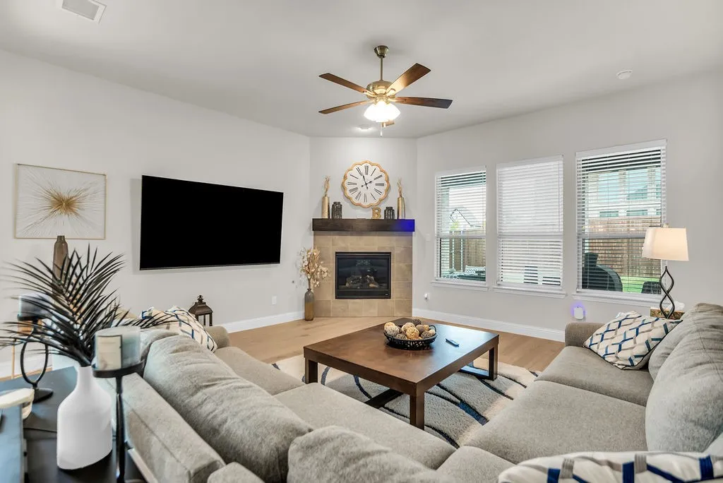 Spacious living area featuring wood-finish flooring, a corner fireplace with a stone surround, and multiple windows