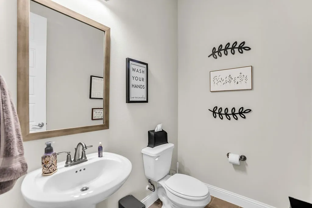 White pedestal sink with a dual-handle faucet, rectangular framed mirror, and a white toilet
