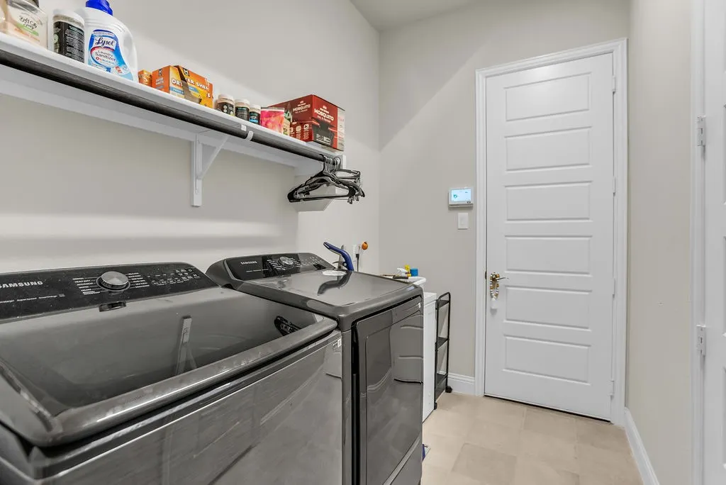 Laundry area featuring light-toned walls, tile flooring, and a white paneled door with a brass-finish handle