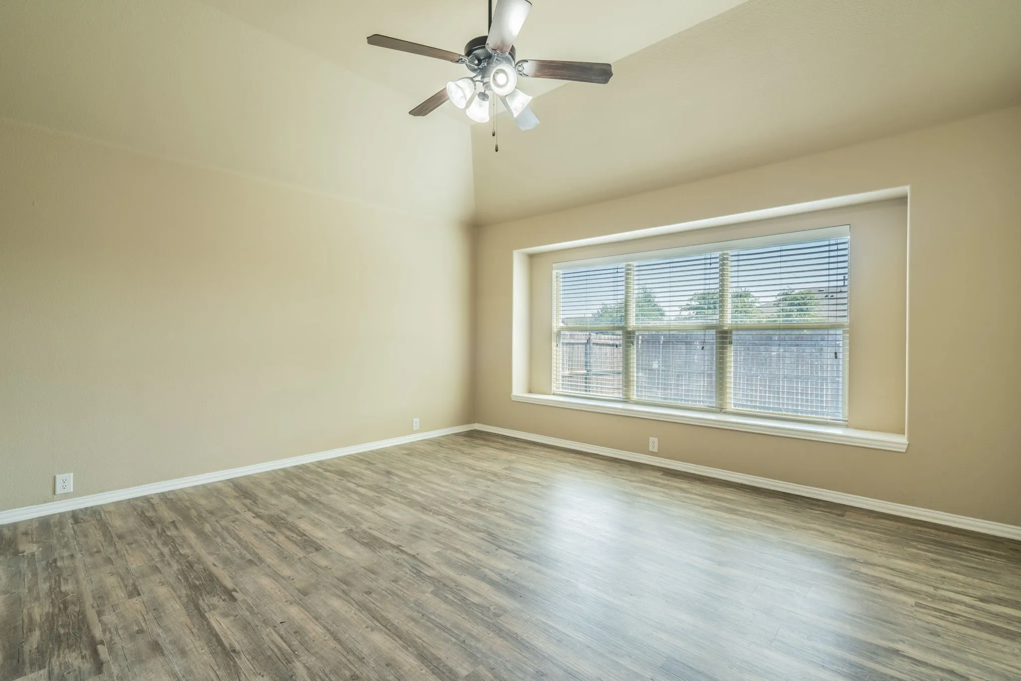 Vaulted ceiling with a ceiling fan, wood-finish flooring, and a large window with blinds