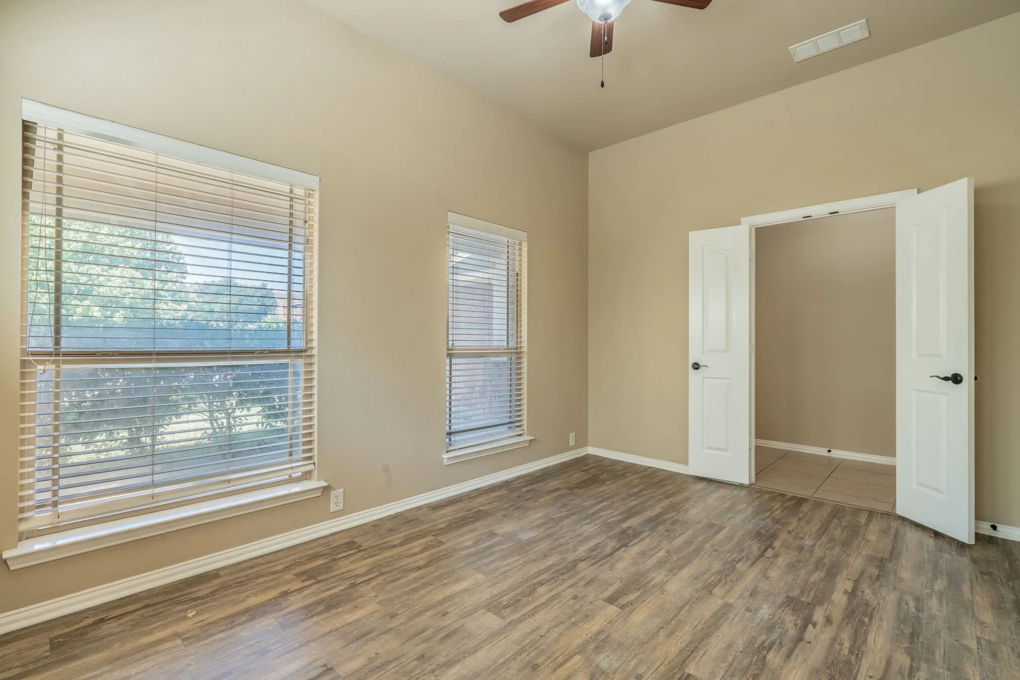 Vaulted ceiling with a ceiling fan, wood-finish flooring, and two double-hung windows with blinds