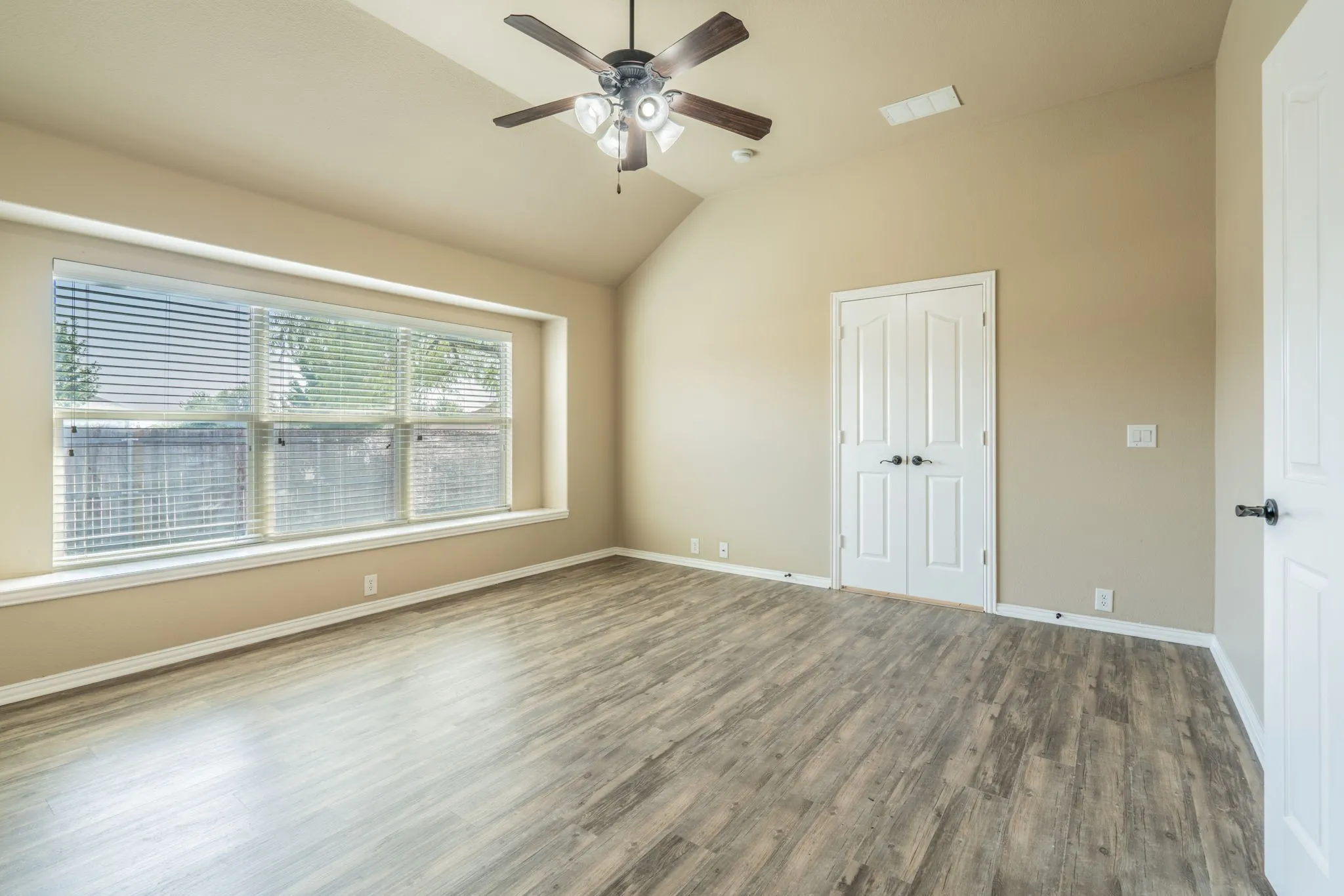 Wood-finish flooring, vaulted ceiling, ceiling fan, large window with blinds, and white double doors