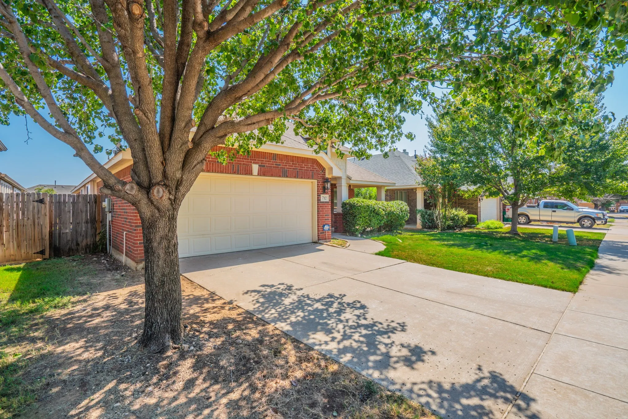 Brick exterior featuring a two-car garage, concrete driveway, and mature landscaping