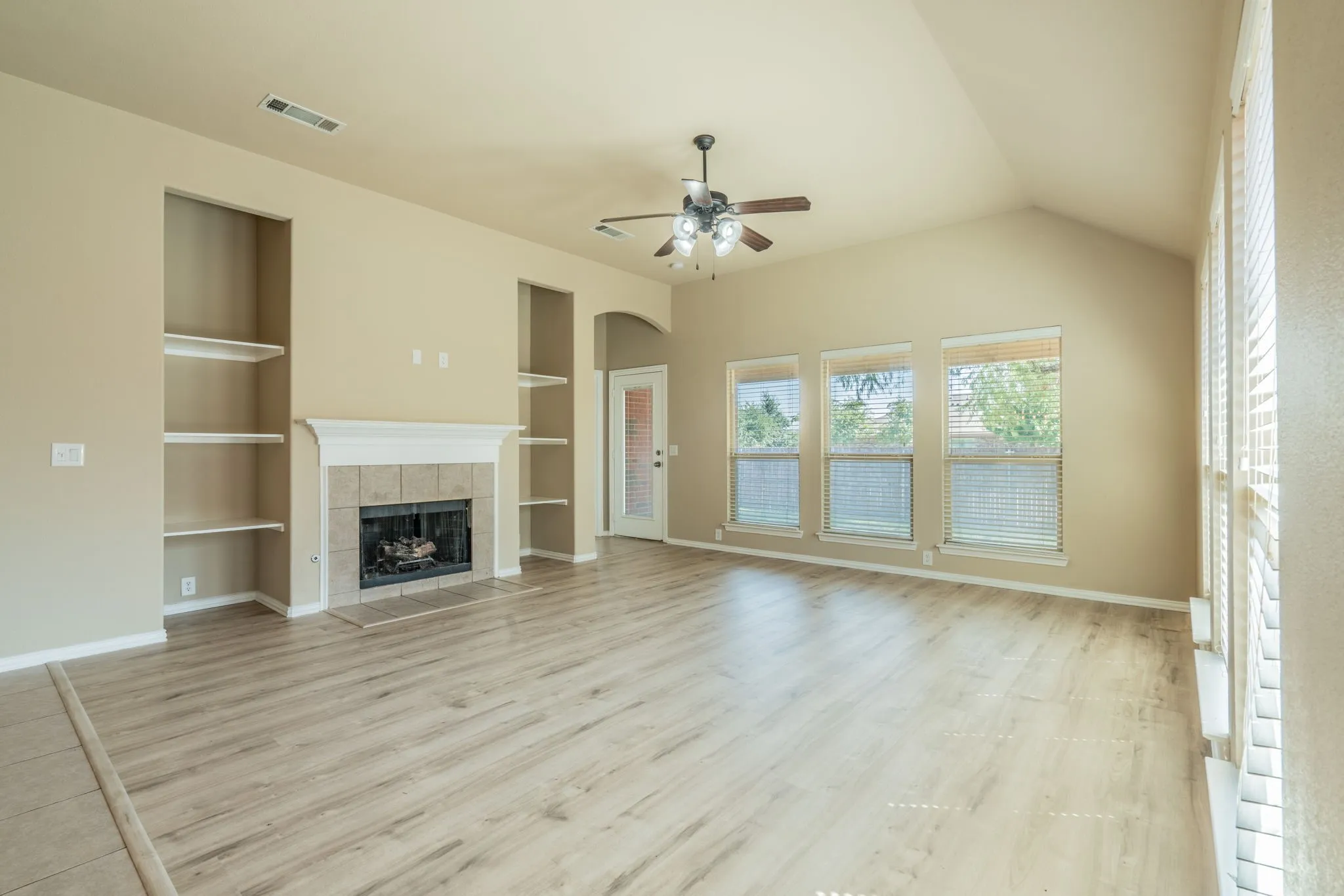 Vaulted ceilings, wood-finish flooring, built-in shelving, stone-surround fireplace, and ceiling fan