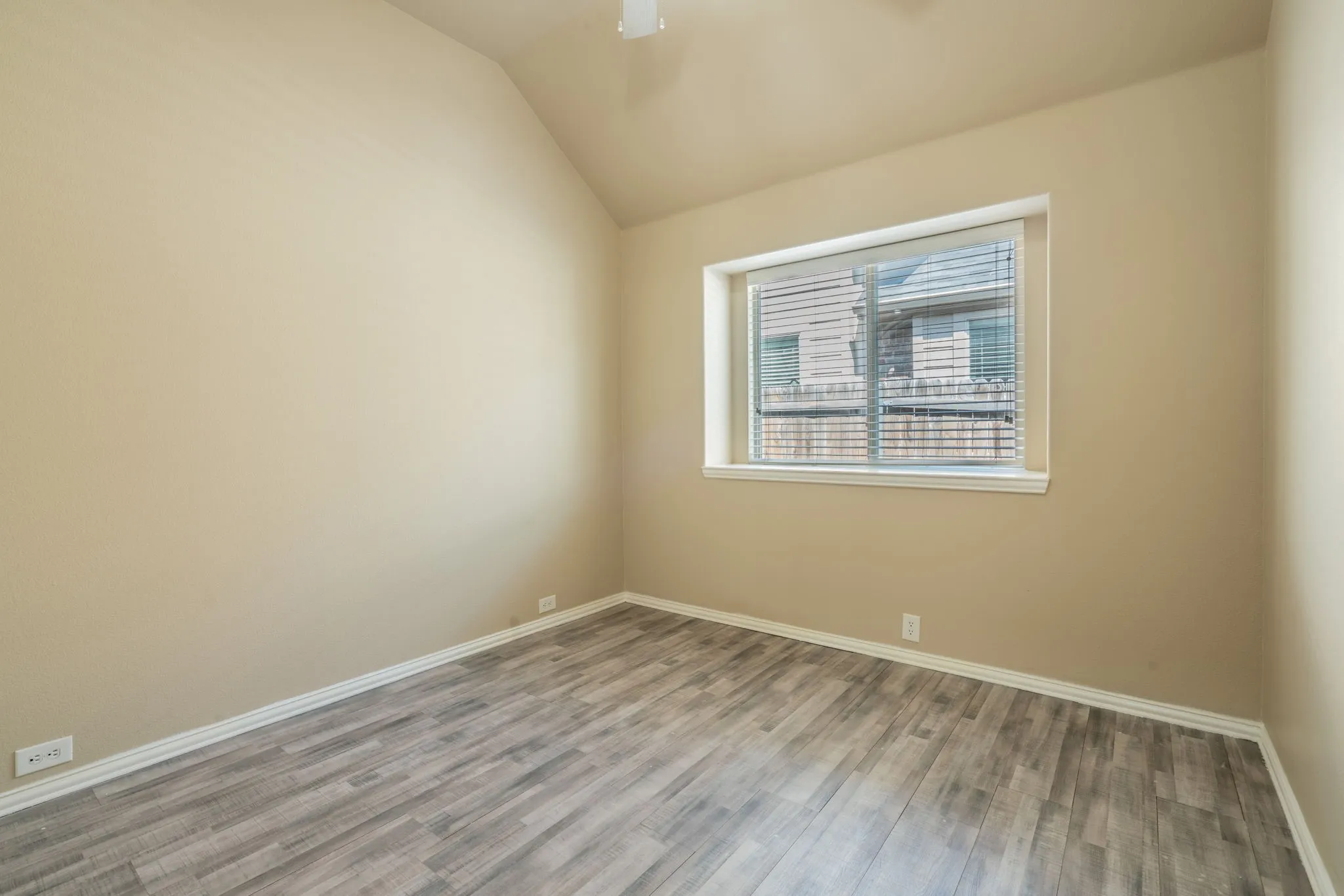 Vaulted ceiling with wood-finish flooring, white trim, and a window with blinds