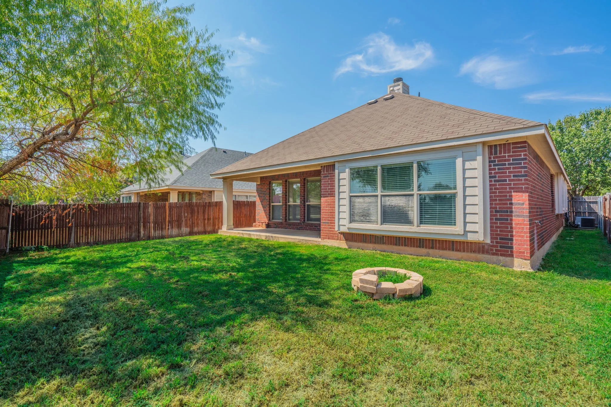 Expansive green lawn featuring a privacy fence, a concrete patio, and a stone-ringed fire pit