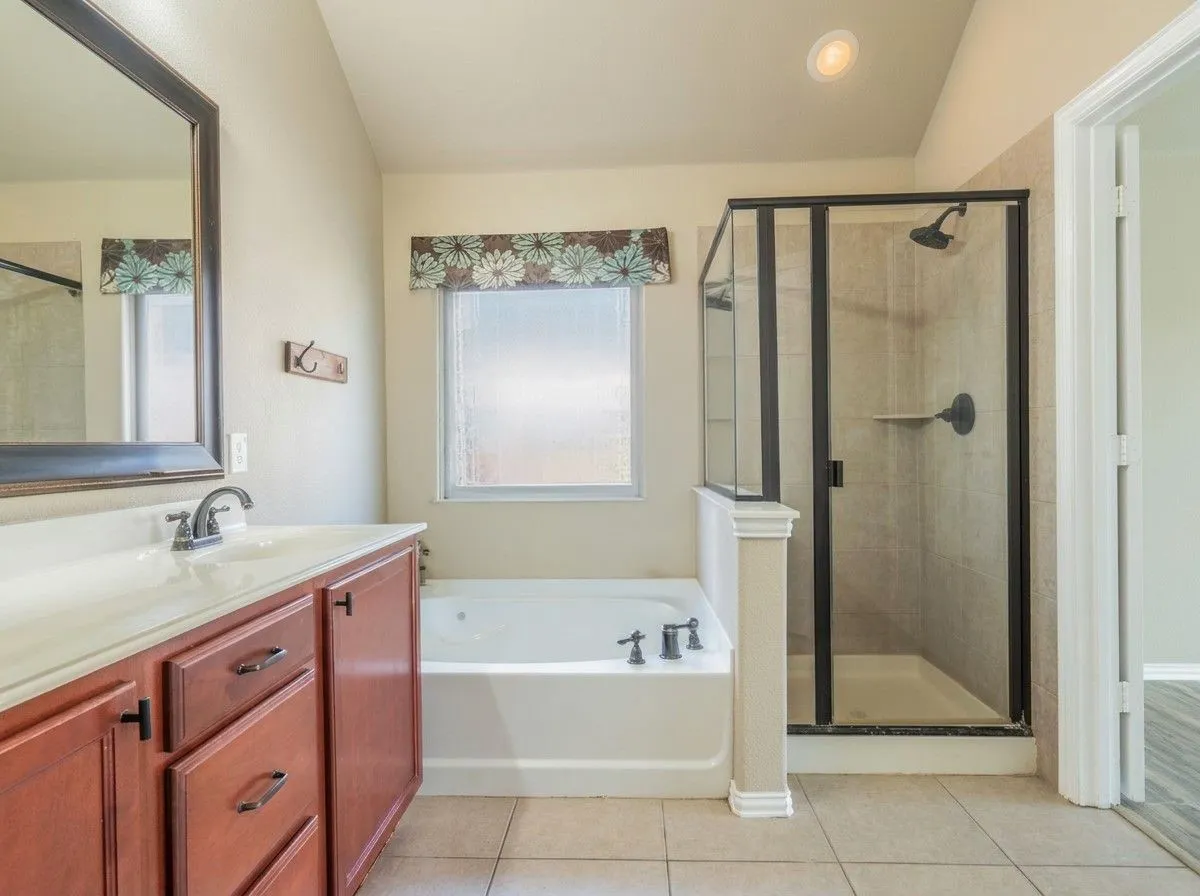 Tile flooring, wood-finish cabinetry, built-in soaking tub, framed glass shower enclosure, and recessed lighting