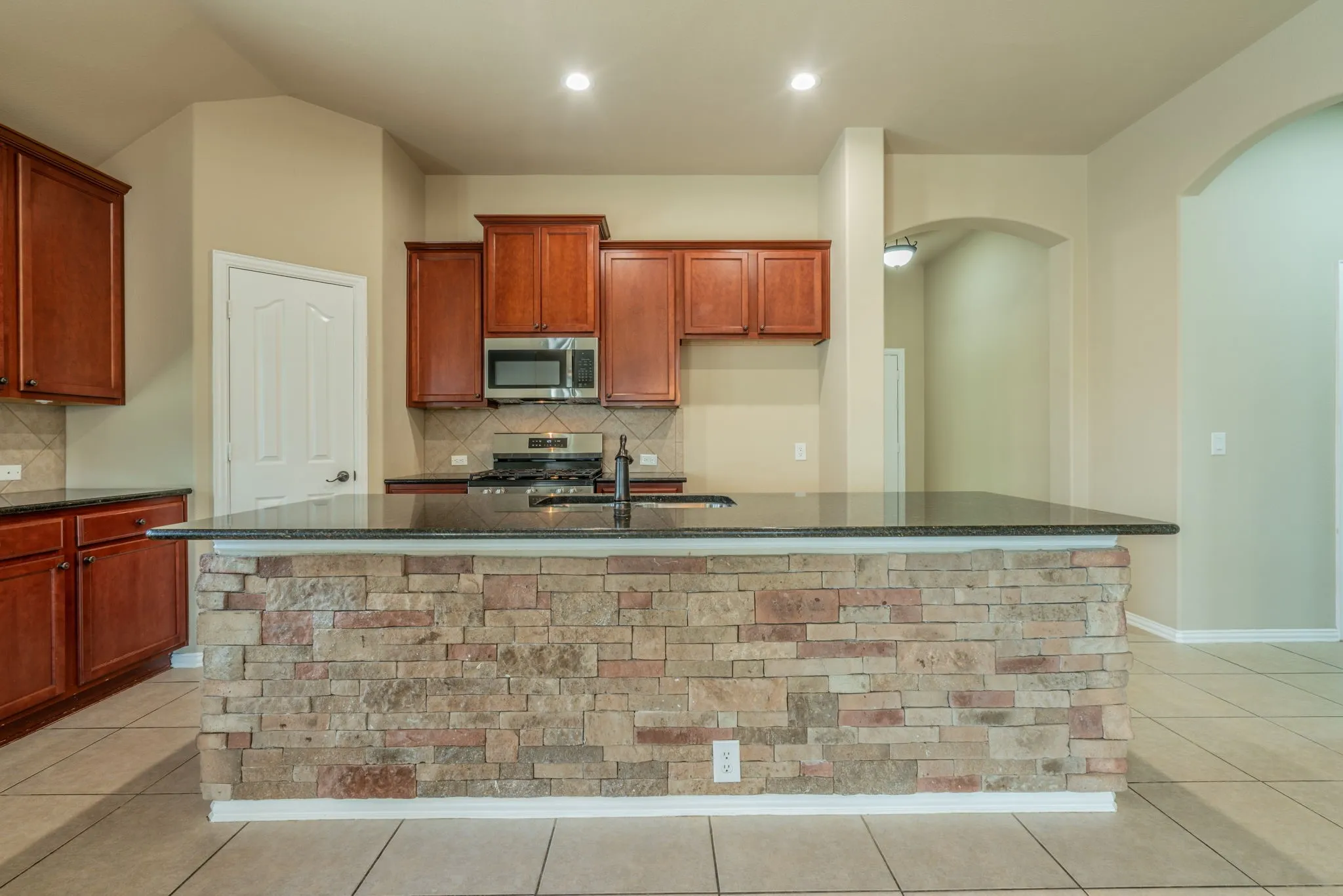 Kitchen island with stone-finish cladding and dark countertop, integrated sink, and stainless steel faucet