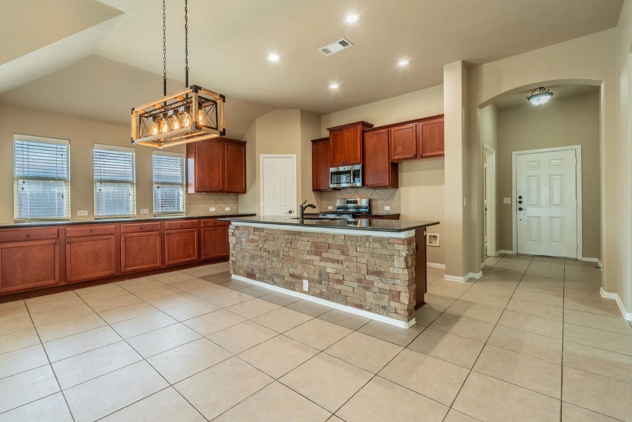 Kitchen with wood cabinetry, dark countertops, tiled flooring, and a stone-clad island