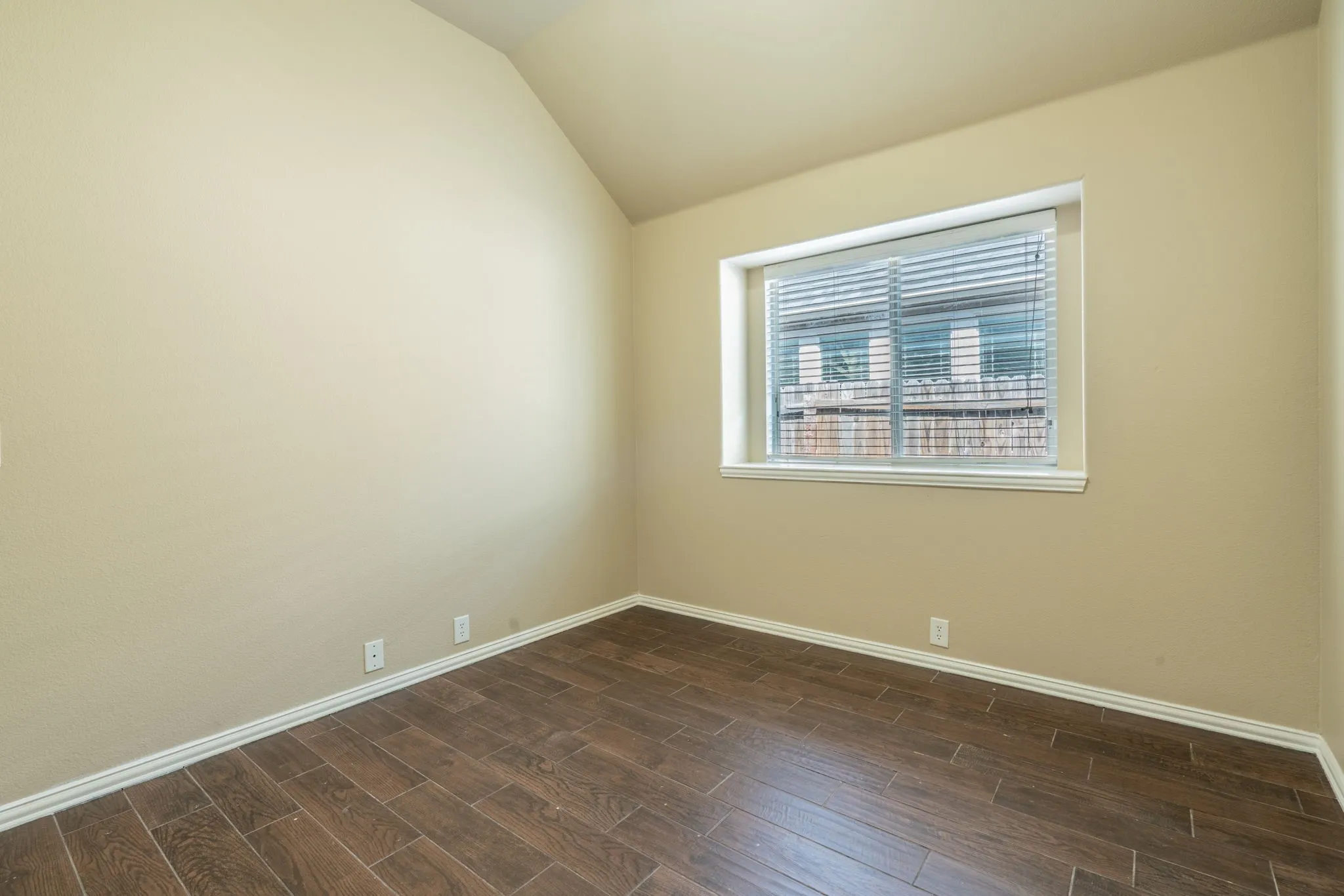 Wood-finish plank flooring, vaulted ceiling, neutral wall paint, and window with blinds