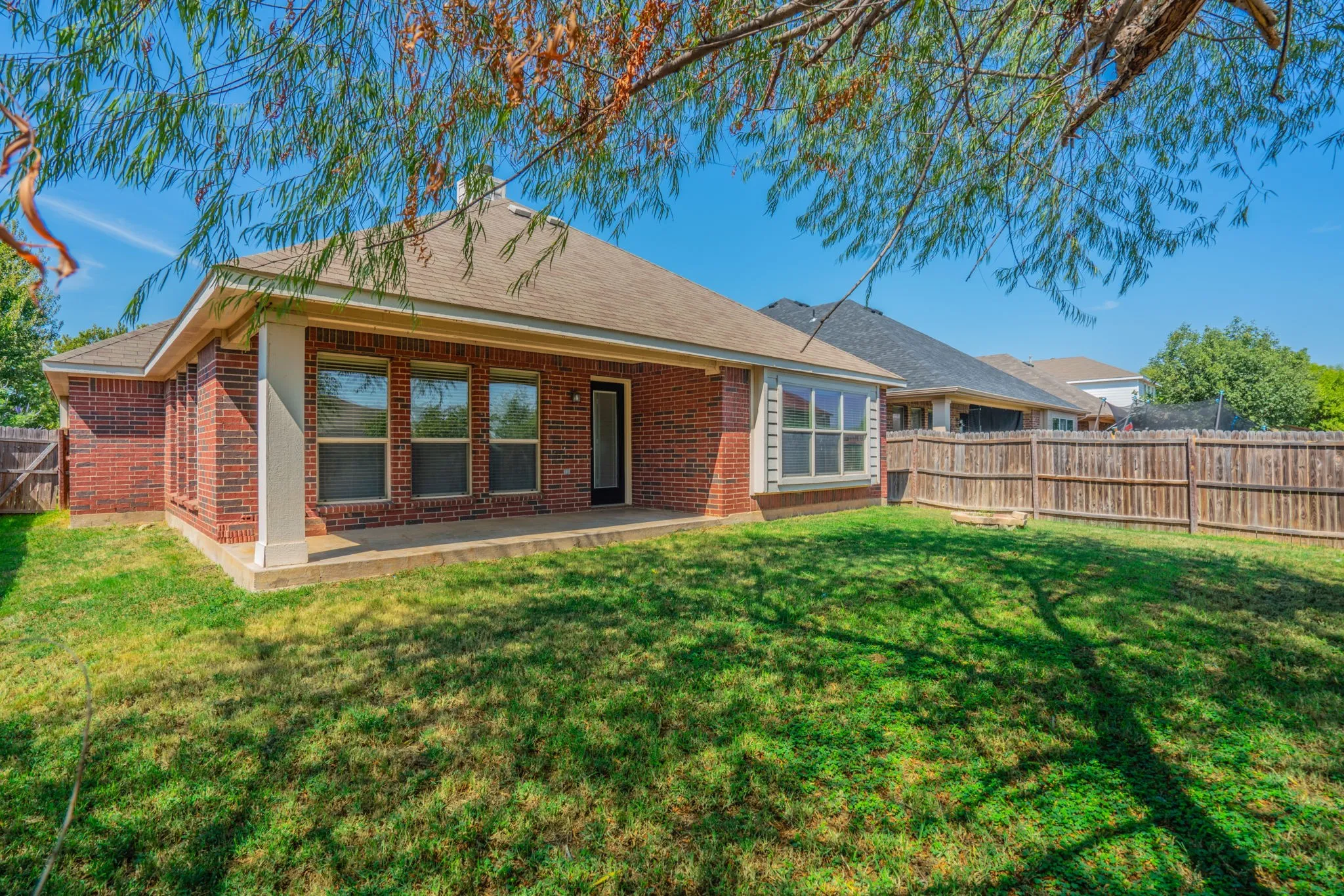 Expansive backyard featuring a manicured lawn, wood fencing, and a covered patio with brick columns
