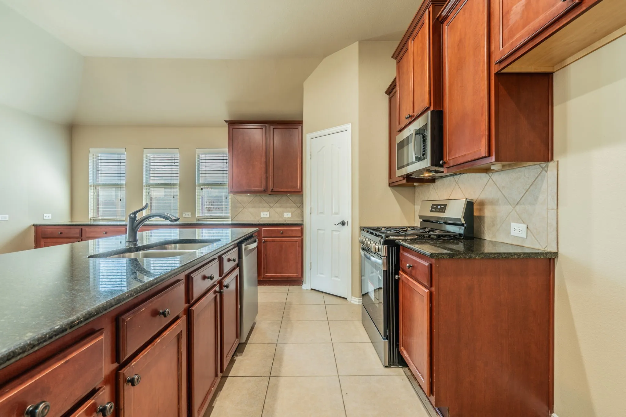Kitchen featuring a large island with sink, wood-finish cabinetry, dark countertops, built-in microwave, and tile flooring