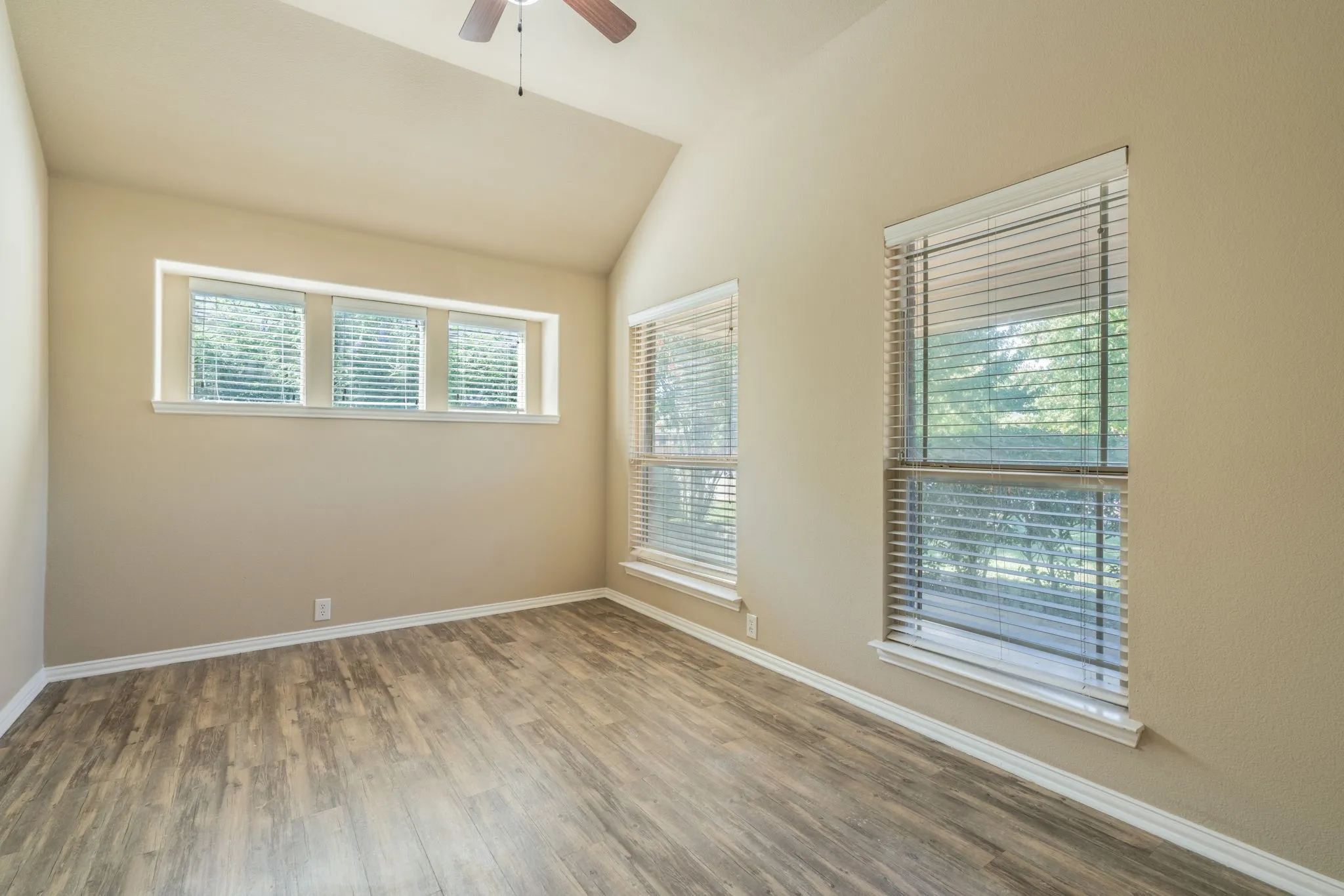 Vaulted ceiling, wood-finish flooring, multiple windows with blinds, ceiling fan