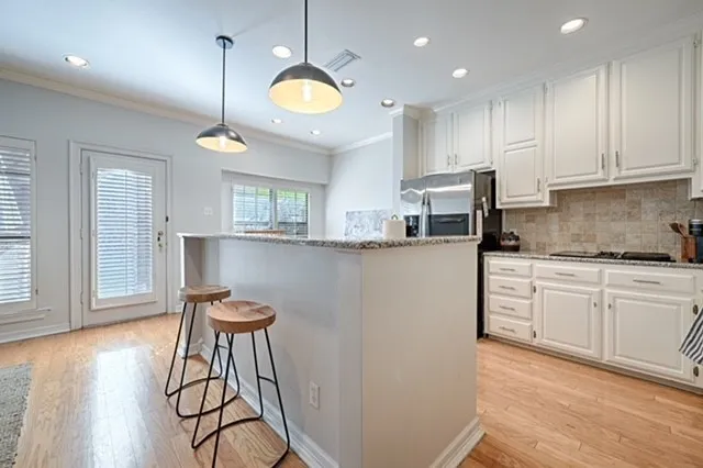 Kitchen featuring light wood-finish flooring, white cabinetry, recessed lighting, pendant lighting, and a granite-finish breakfast bar