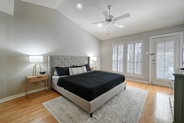 Vaulted ceiling with a ceiling fan, wood-finish flooring, multiple windows with plantation shutters, and a glass-paneled door