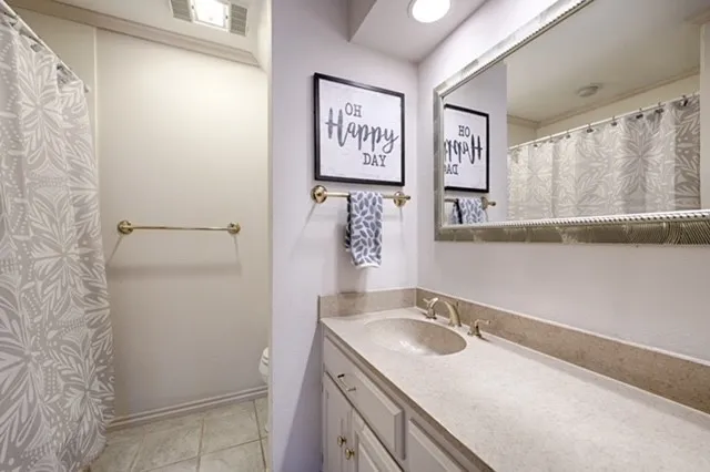 Vanity with an integrated sink and light-colored countertop, framed wall mirror, and tile flooring