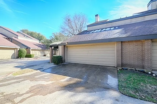Attached garage with roll-up door, brick facade detailing, and asphalt shingle roofing