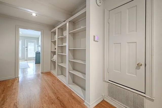 Hardwood flooring, recessed lighting, white built-in shelving, white paneled door, and a white ceiling with exposed beams