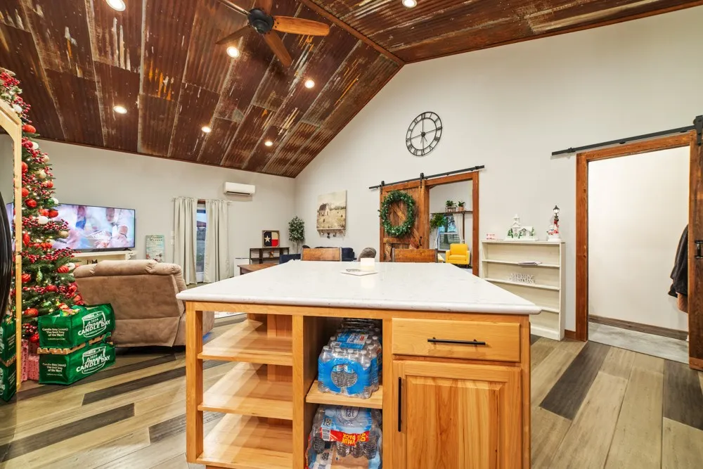 Vaulted ceiling with corrugated metal finish, recessed lighting, wood-finish flooring, central island with light-toned countertop, and barn-style sliding doors