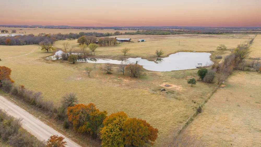 Expansive rural landscape featuring two ponds, mature trees, and open fields with a dirt road