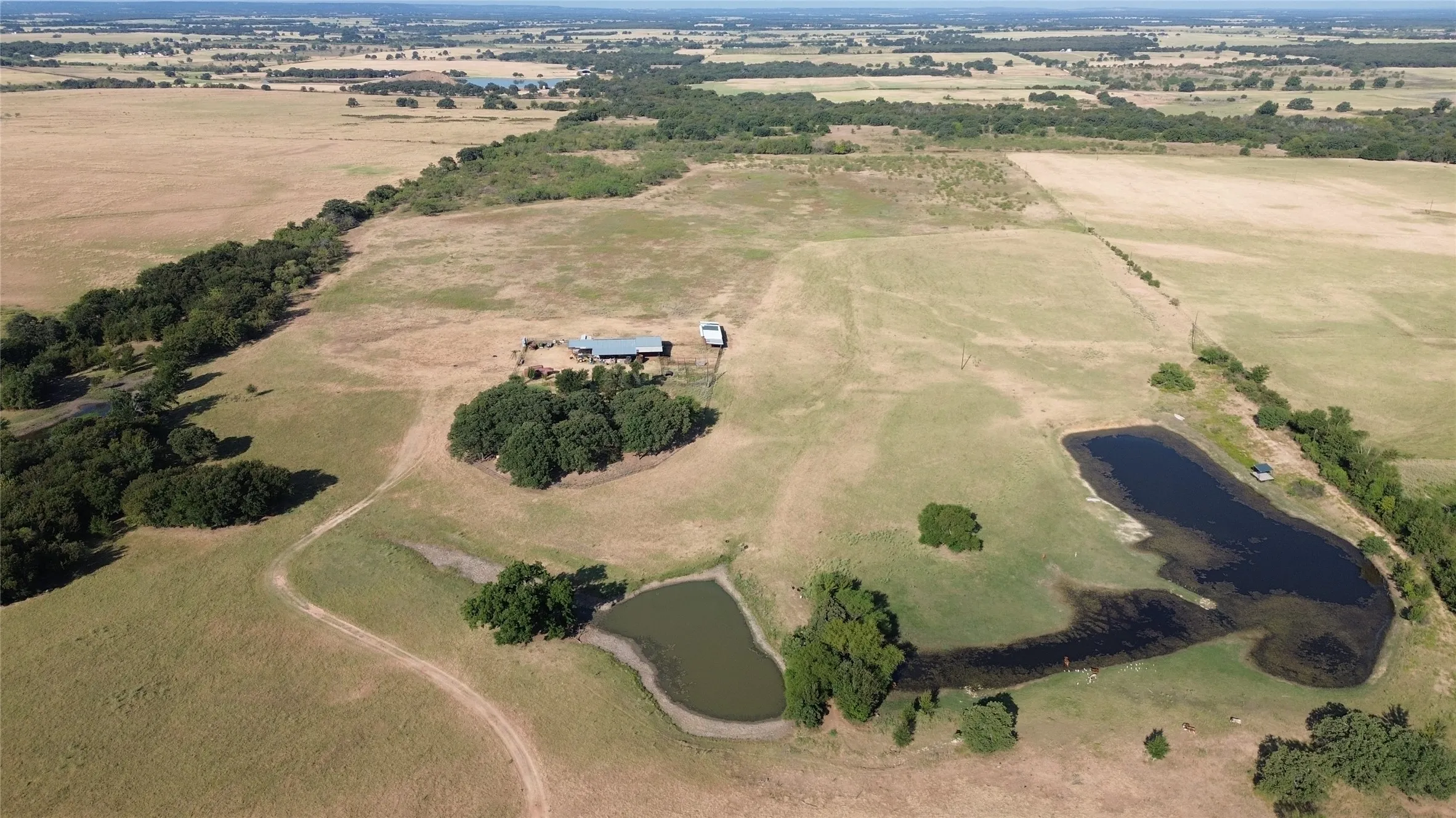 Expansive rural property featuring multiple ponds, scattered mature trees, and a distant residential structure