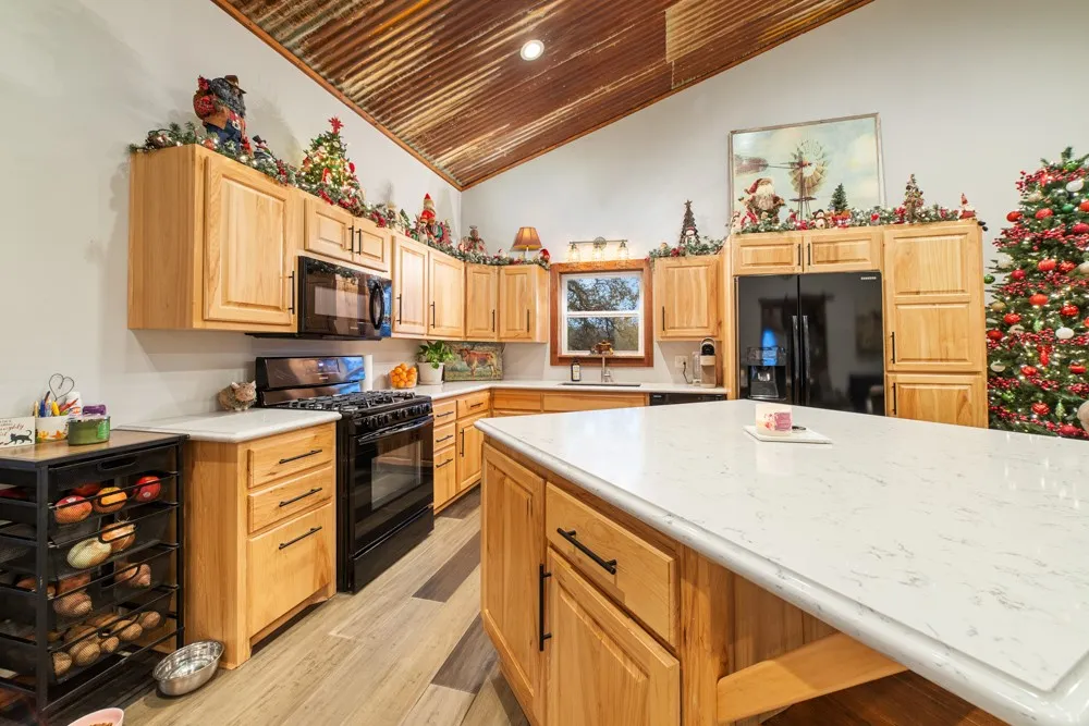 Kitchen featuring wood cabinetry, white countertops, black appliances, a central island, and wood-finish flooring