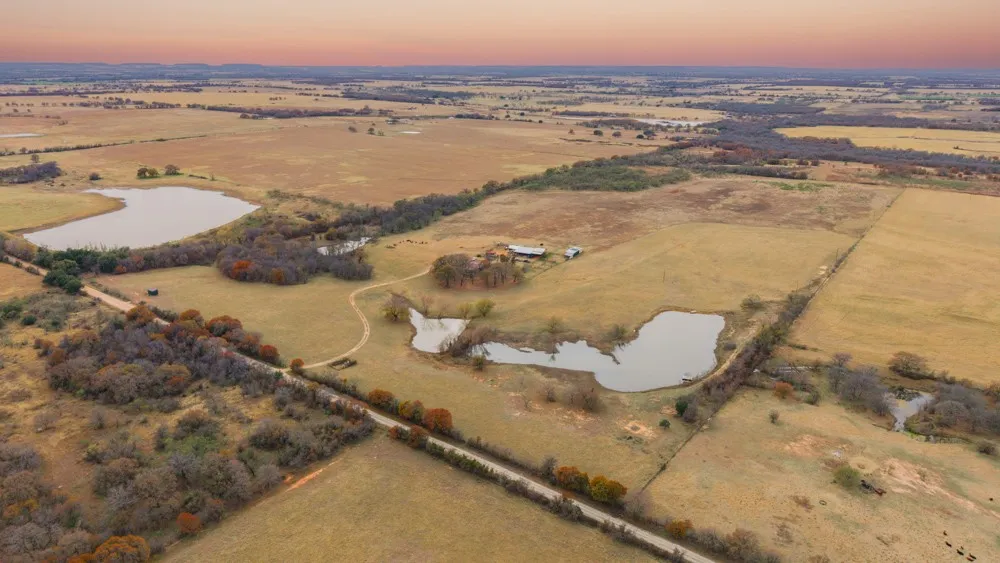 Expansive acreage featuring multiple ponds, a winding unpaved road, mature trees, and agricultural fields