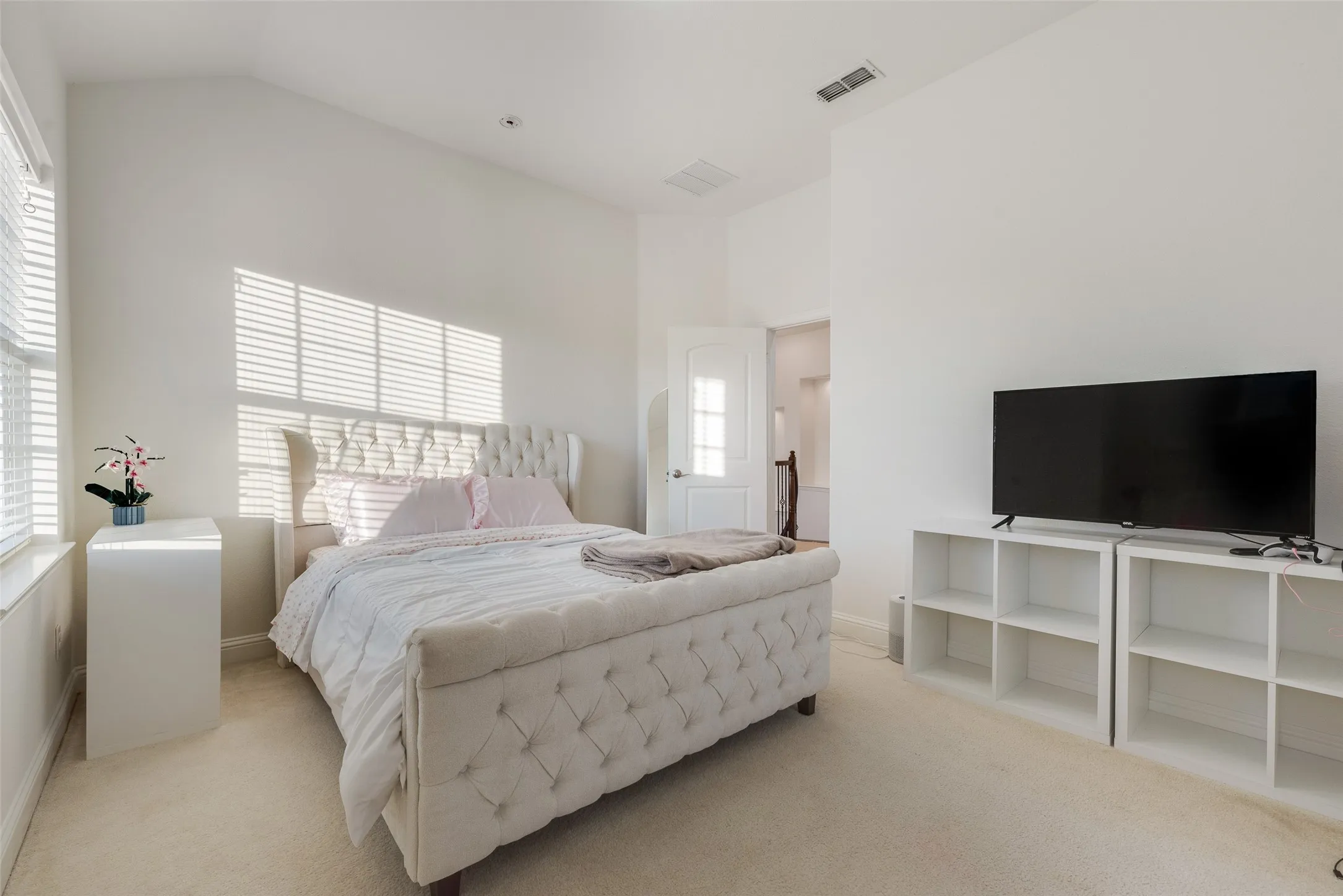 Vaulted ceiling, neutral wall paint, carpet flooring, window with blinds, white paneled door