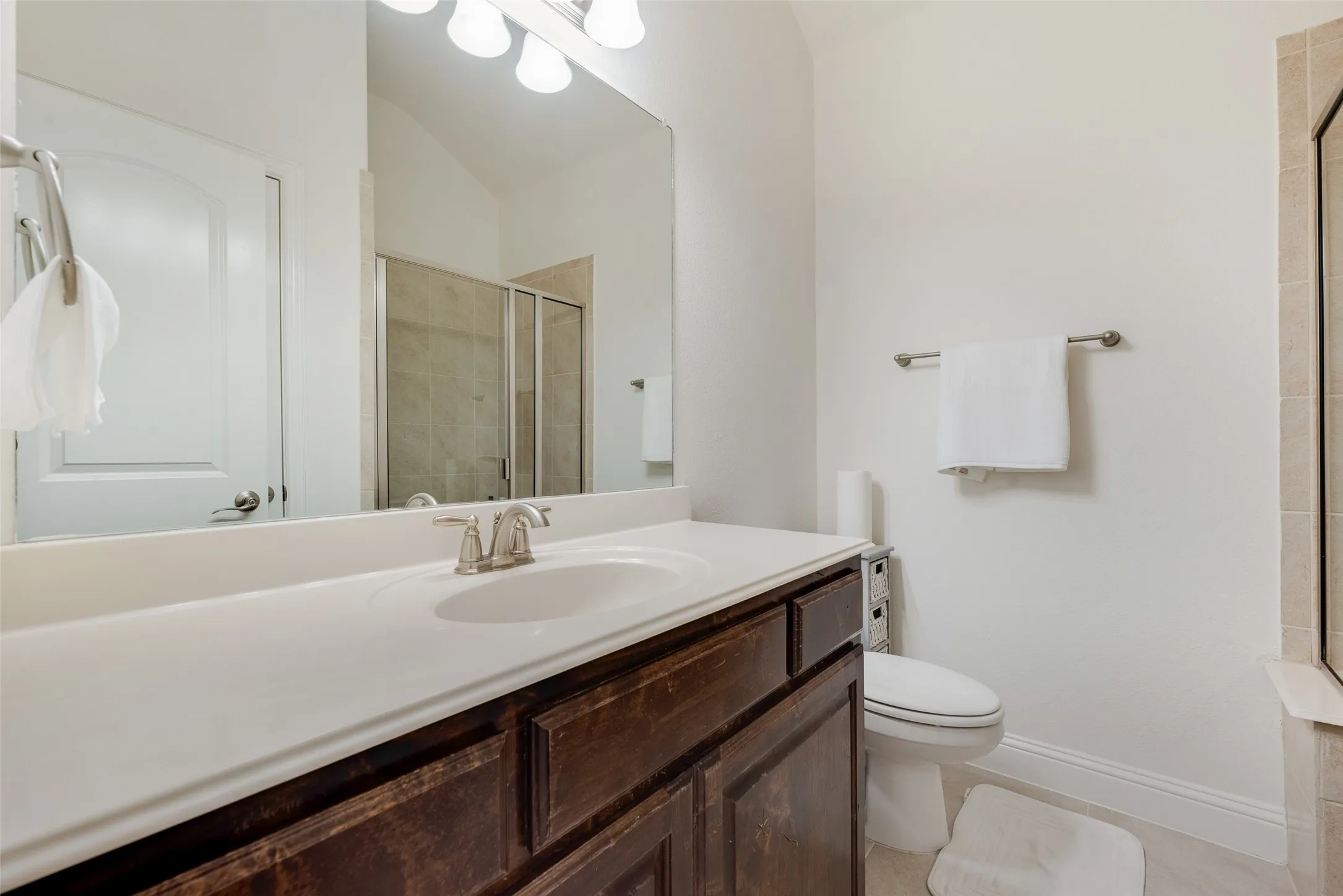 Vanity with an integrated sink, brushed nickel faucet, wood-finish cabinetry, and a shower with a glass enclosure