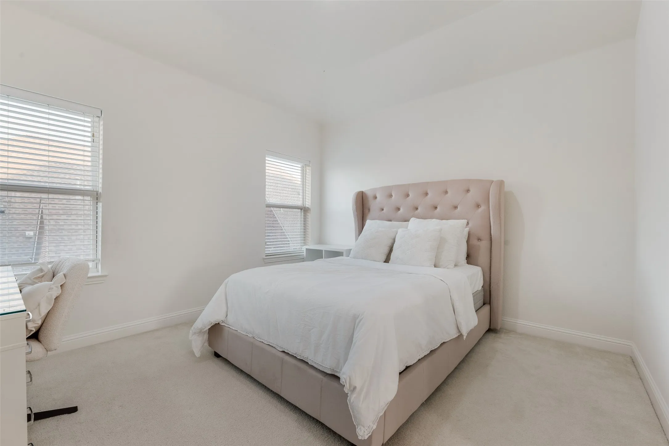 Light-toned carpet flooring, two windows with horizontal blinds, and clean white wall finishes
