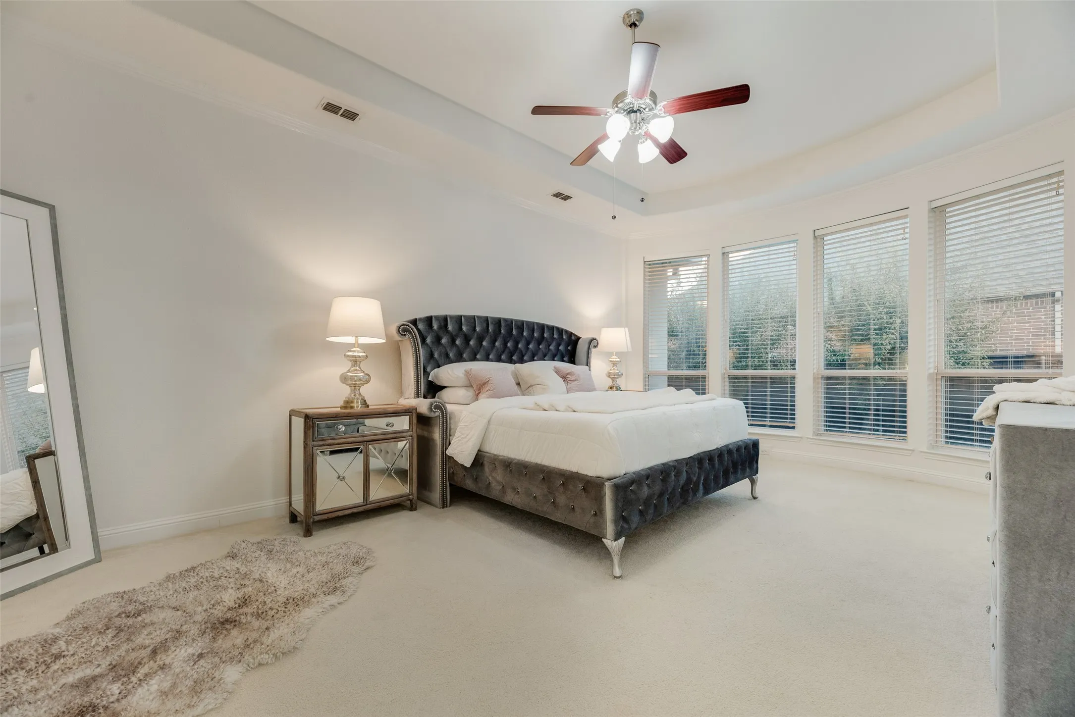Recessed lighting, ceiling fan with light fixture, tray ceiling, multiple windows with blinds, and light-colored carpeting