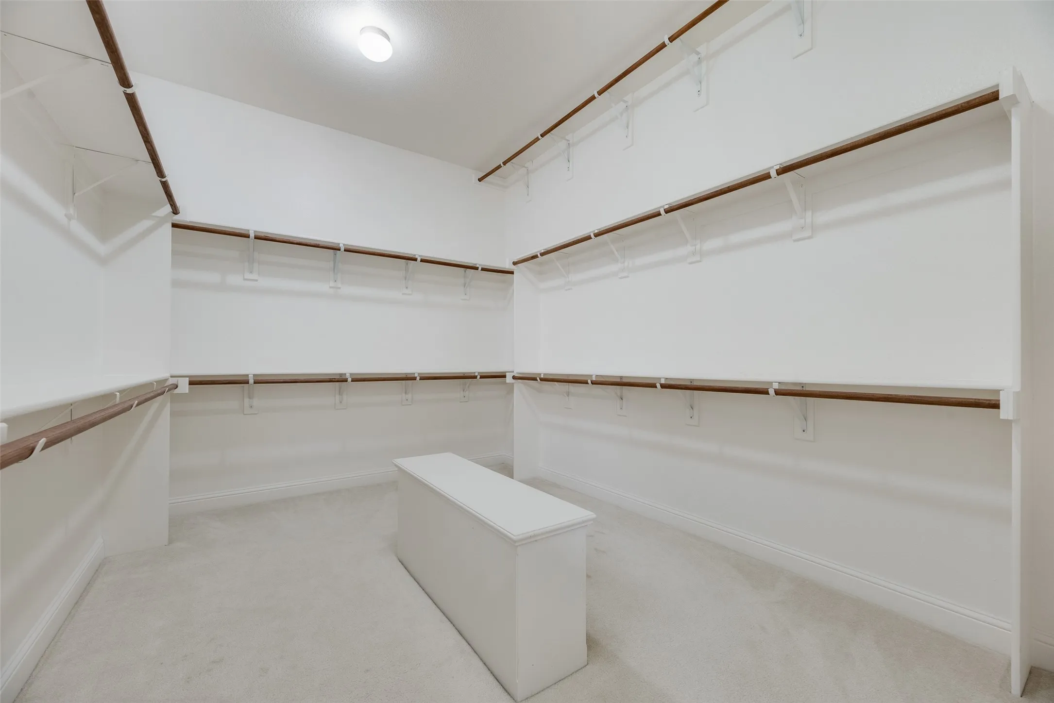 Spacious walk-in closet featuring extensive built-in shelving, multiple hanging rods, and light-toned carpeting