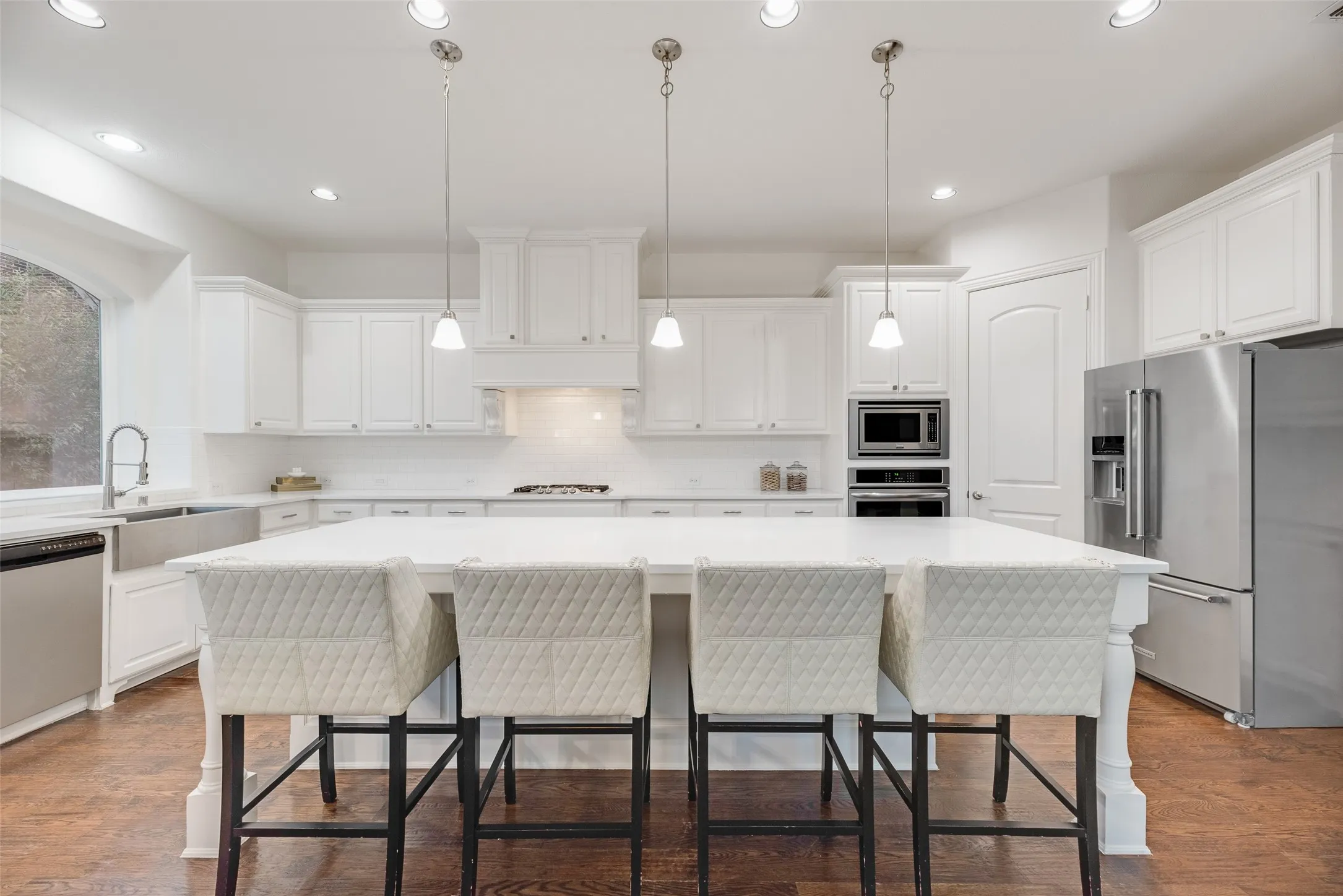 White shaker cabinetry with crown molding, stainless steel appliances, a center island with pendant lighting, and wood-finish flooring