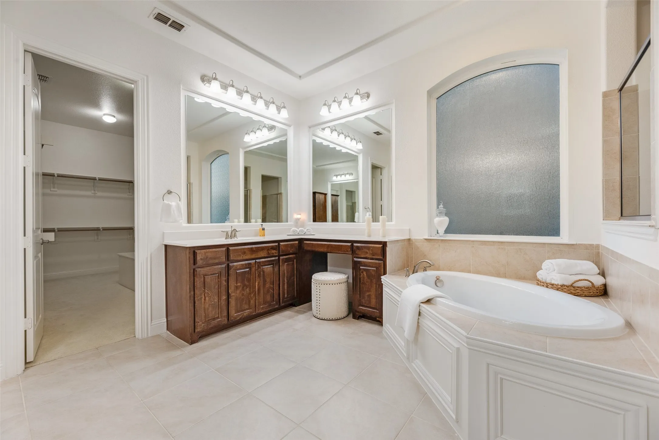 Tile flooring, built-in bathtub, dual vanity with wood cabinetry, and a privacy window