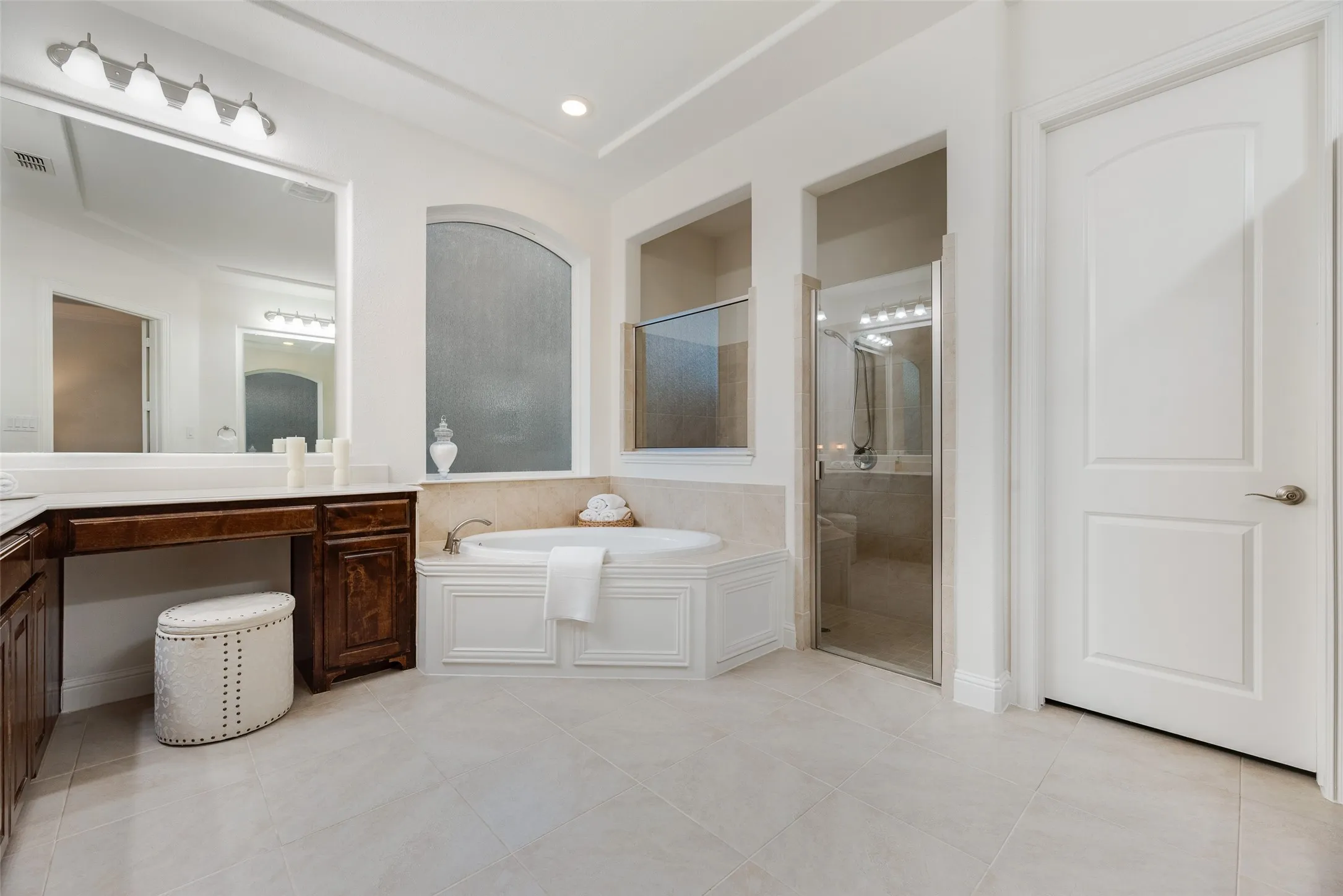 Corner soaking tub, separate shower with glass enclosure, dual vanity with wood-finish cabinetry, and neutral tile flooring