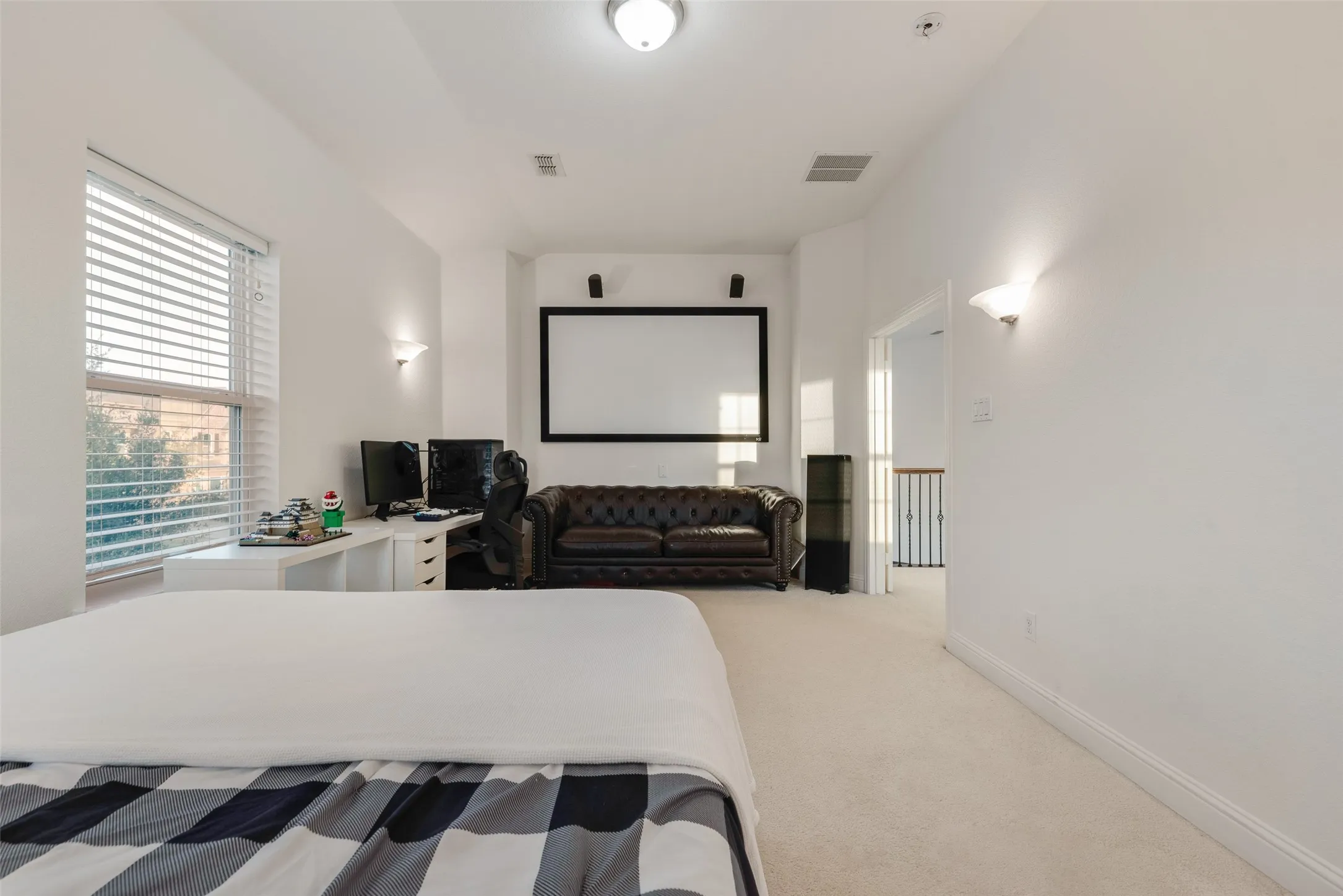 Wall-mounted projection screen, recessed lighting, and sconce lighting fixtures illuminate this carpeted room